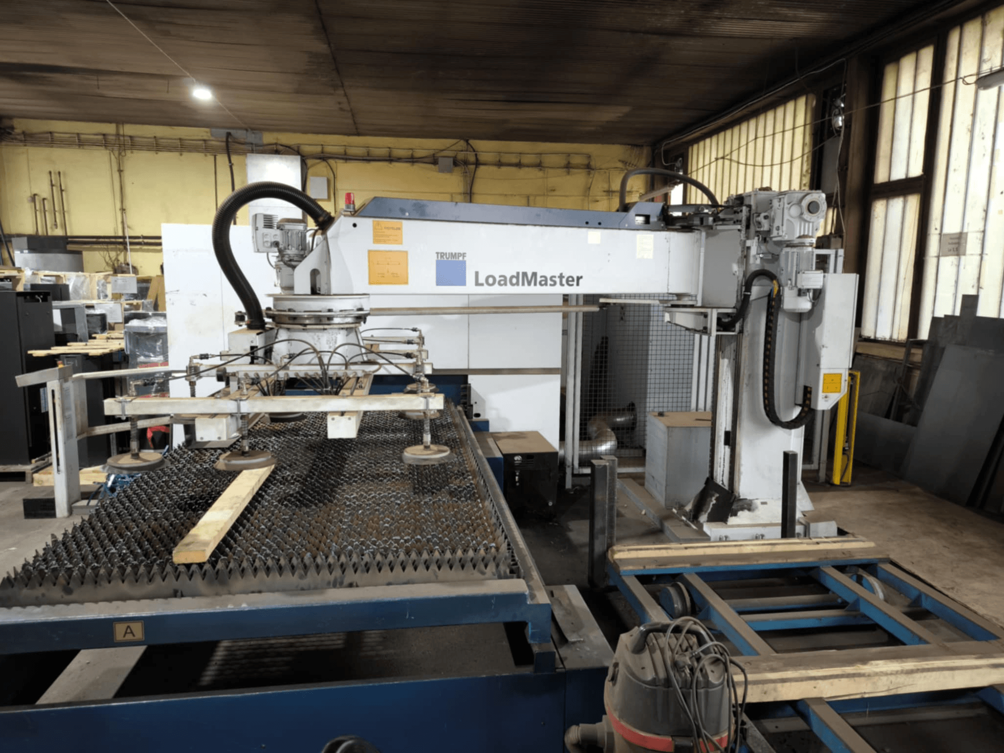 TRUMPF TRULASER 3030 FIBER snijmachine, vooraanzicht, met het LoadMaster systeem en geplaatst op een werktafel met rooster.