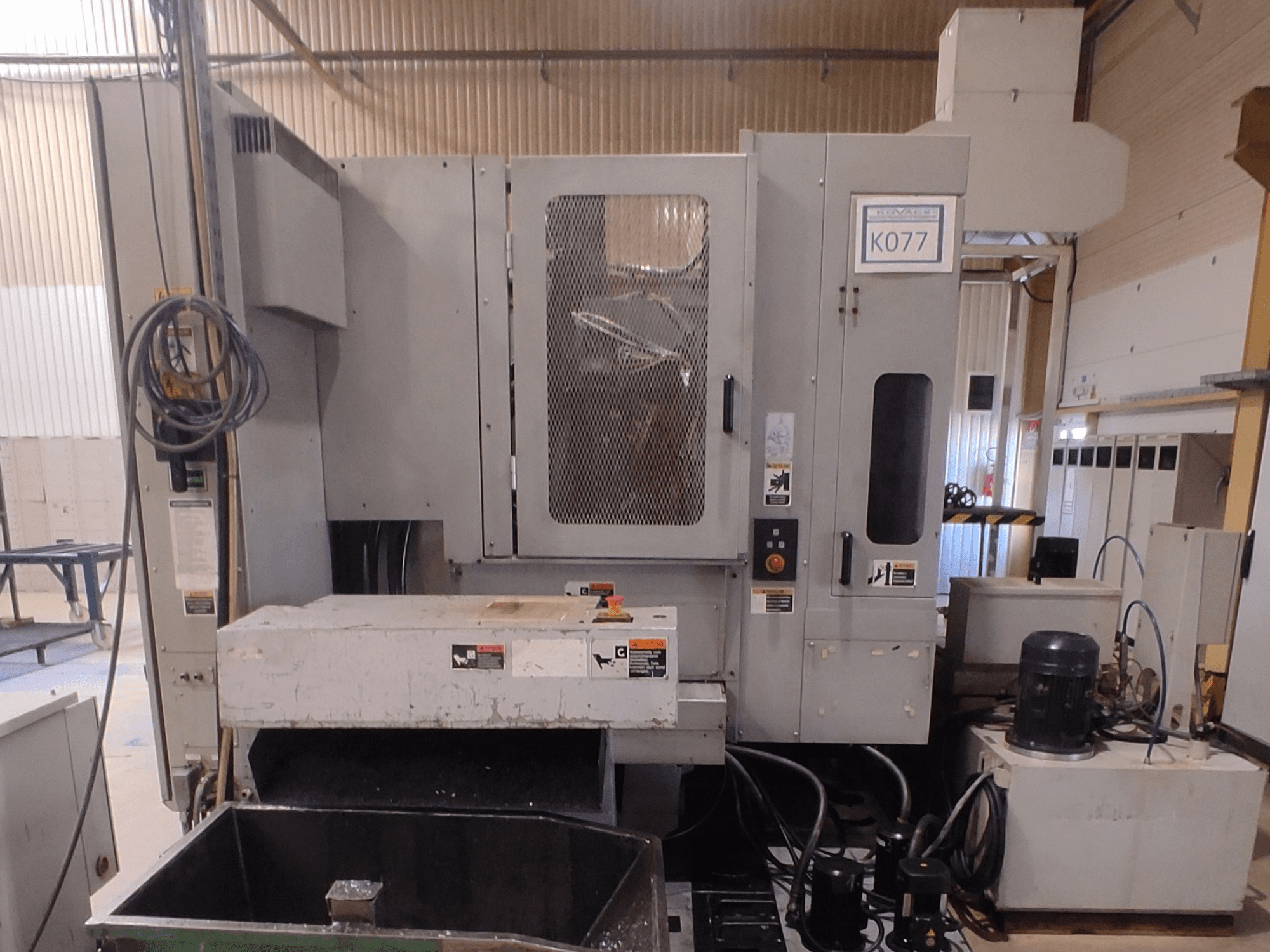 Grijze industriële CNC machine met een grote werktafel, zijaanzicht, met bedieningspaneel en koelvloeistofreservoir, model K077.