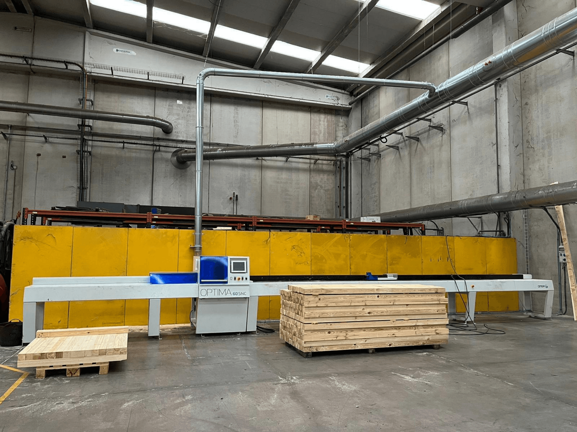 Vooraanzicht van de OPTIMA 60SNC 6200 CE-optimalisatiezaag, met houten pallets en gele veiligheidshekken op de achtergrond.