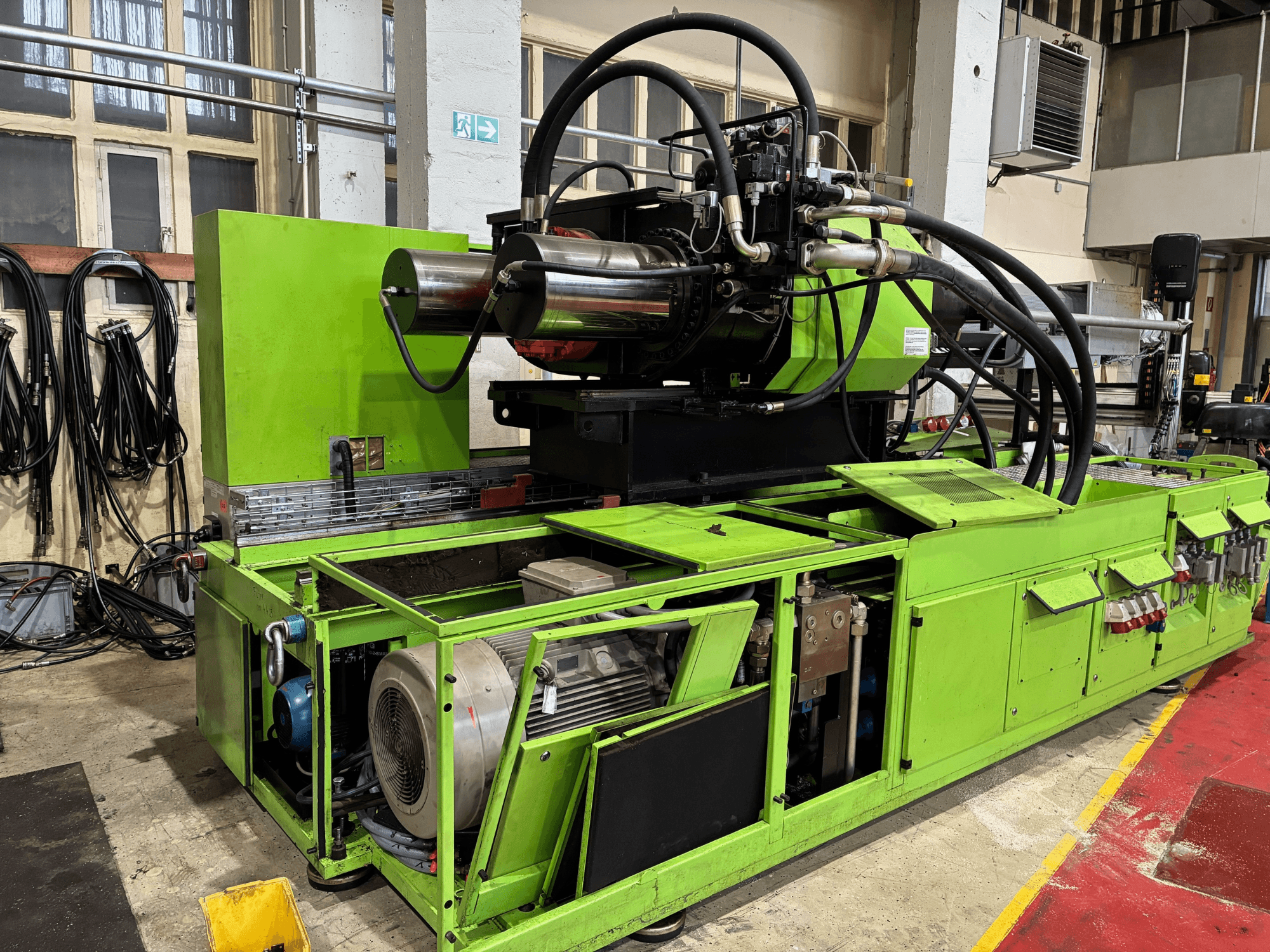 Groene industriële machine met hydraulisch systeem, vooraanzicht, met motor en verschillende bedieningspanelen.