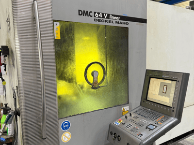 DMC 64 V lineair van Deckel Maho, vooraanzicht van machine met bedieningspaneel en geelgetint venster dat de mechanismen binnenin toont.