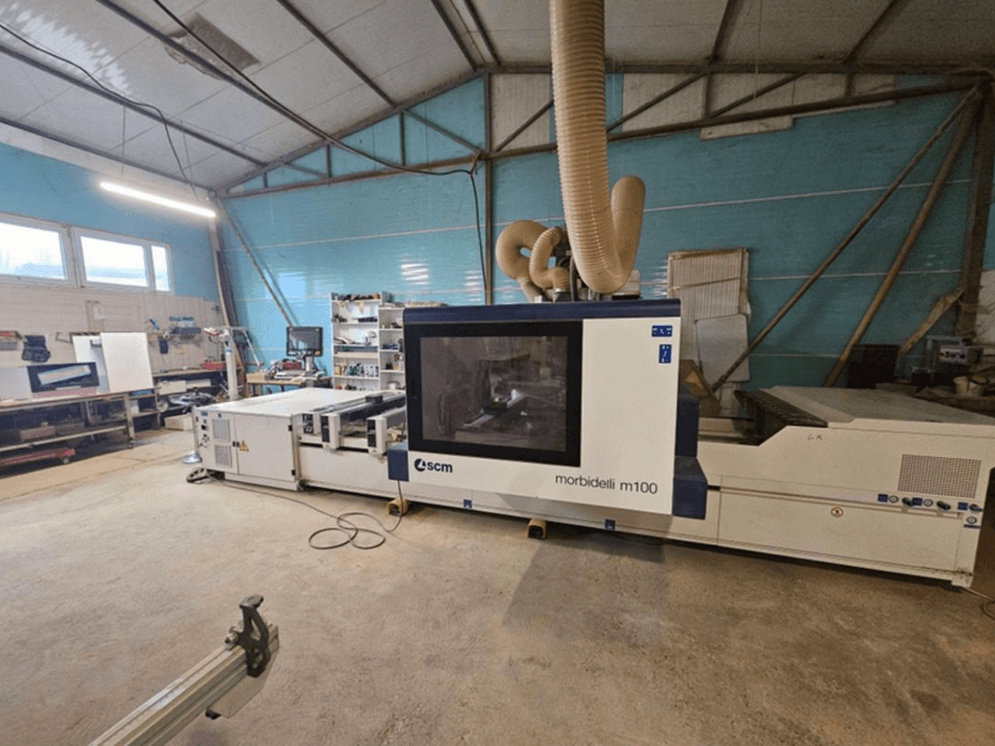 SCM MORBIDELLI M 100 CNC-bewerkingscentrum in een werkplaats, vooraanzicht met stofafzuiging en de omliggende werkplekinrichting.