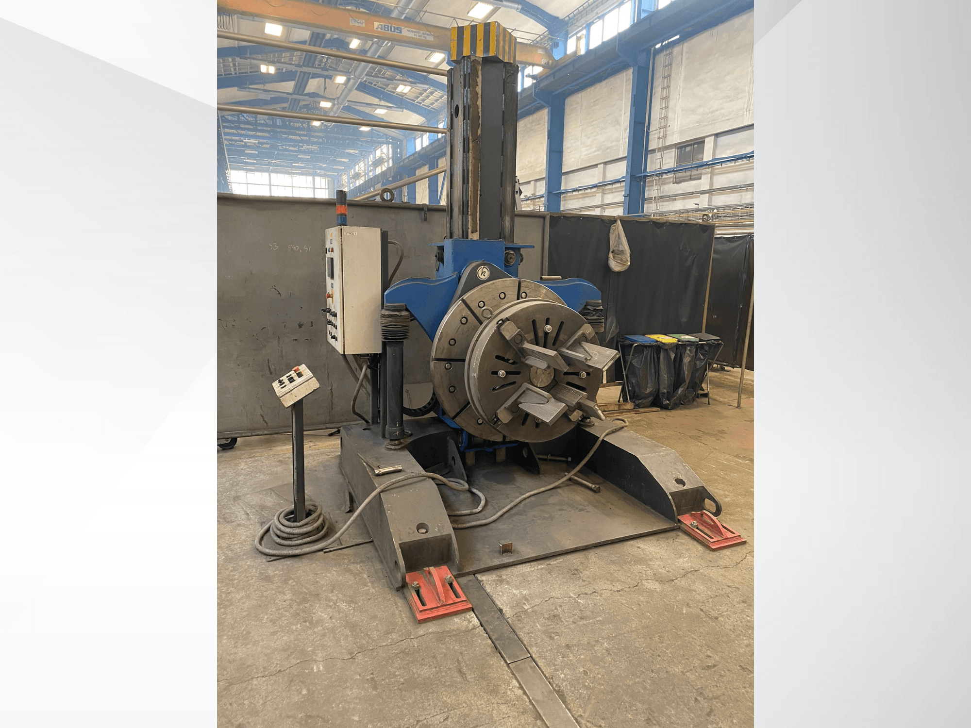 Blauwe industriële draaibank met een ronde roterende kop en bedieningspaneel, zijaanzicht, in een werkplaats.