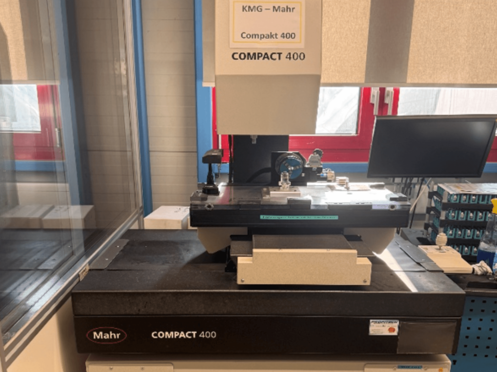 De MAHR Compakt 400-coördinatenmeetmachine, gezien vanaf de voorkant, met meetcomponenten en een monitor ernaast.