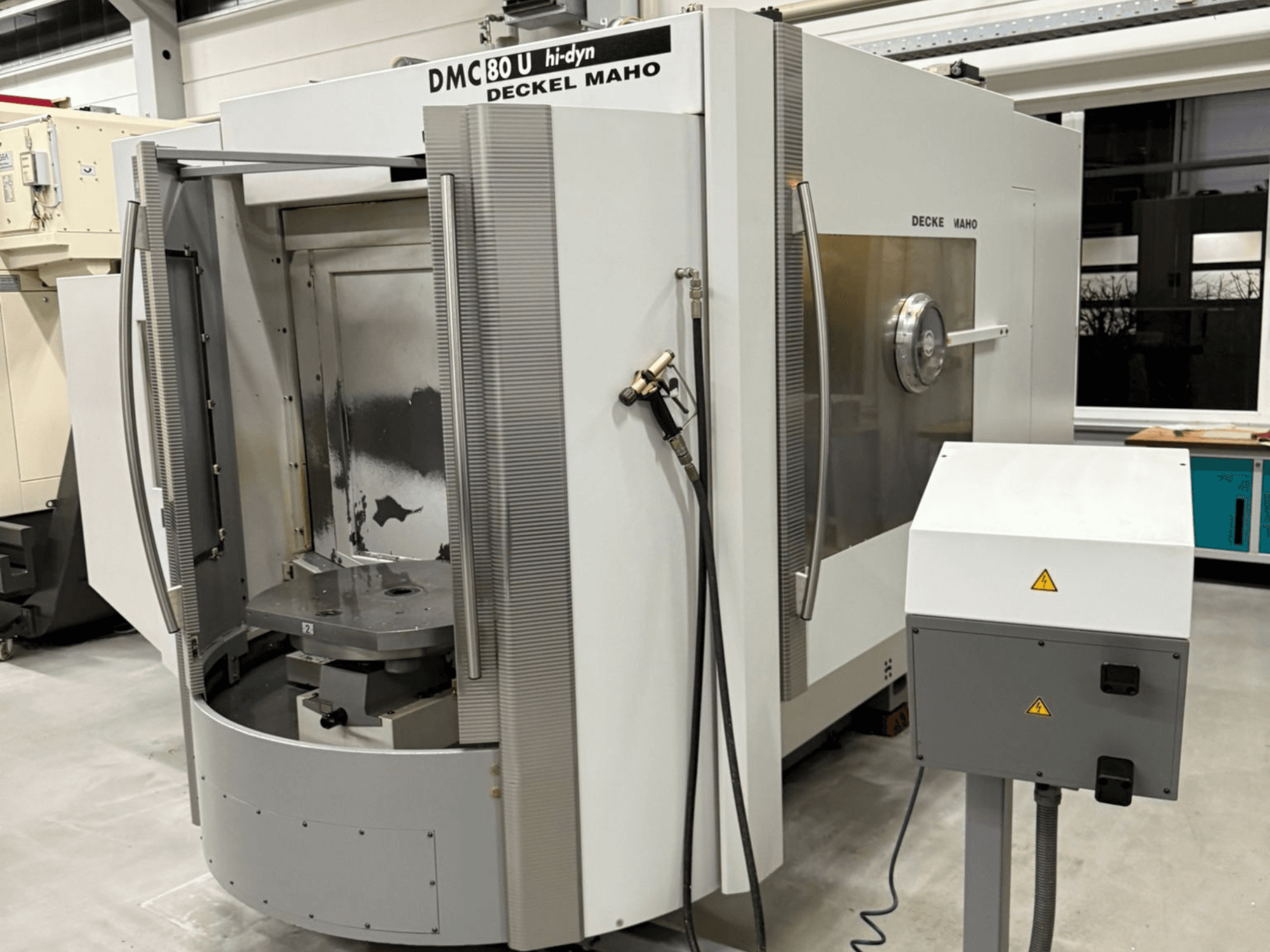 Vooraanzicht van een Deckel Maho DMC 80 U CNC hogesnelheidsfreesmachine, met een open toegangsdeur en bedieningspaneel aan de zijkant.