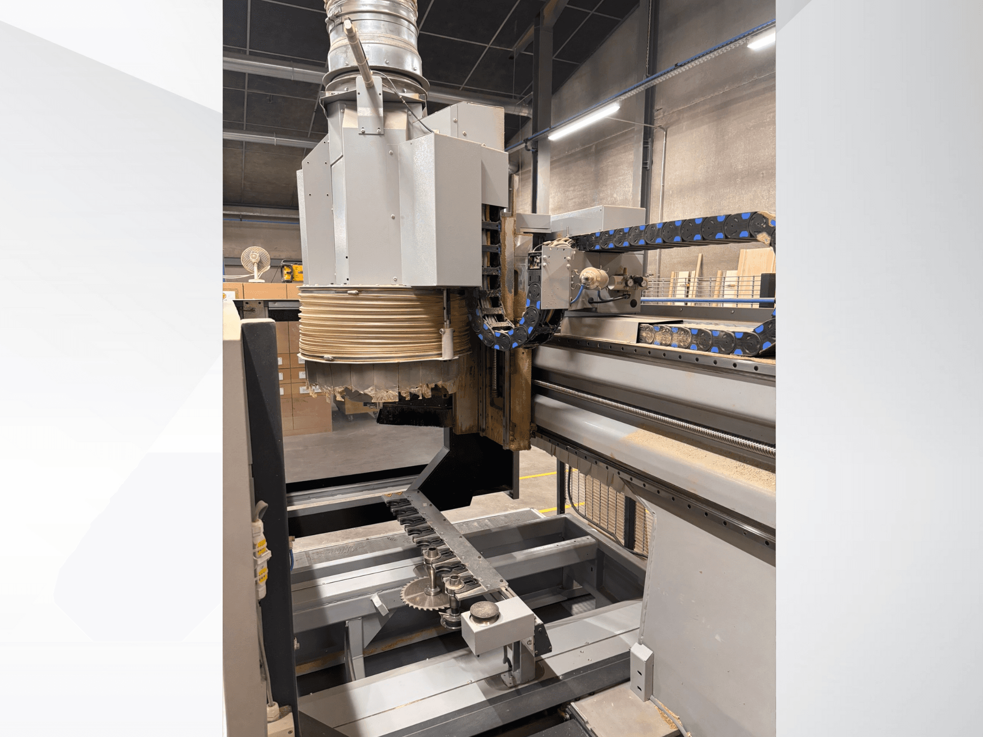 CNC bovenfreesmachine met een grote spindel en transportband, zijaanzicht, met houtsnijgereedschappen en machineonderdelen.