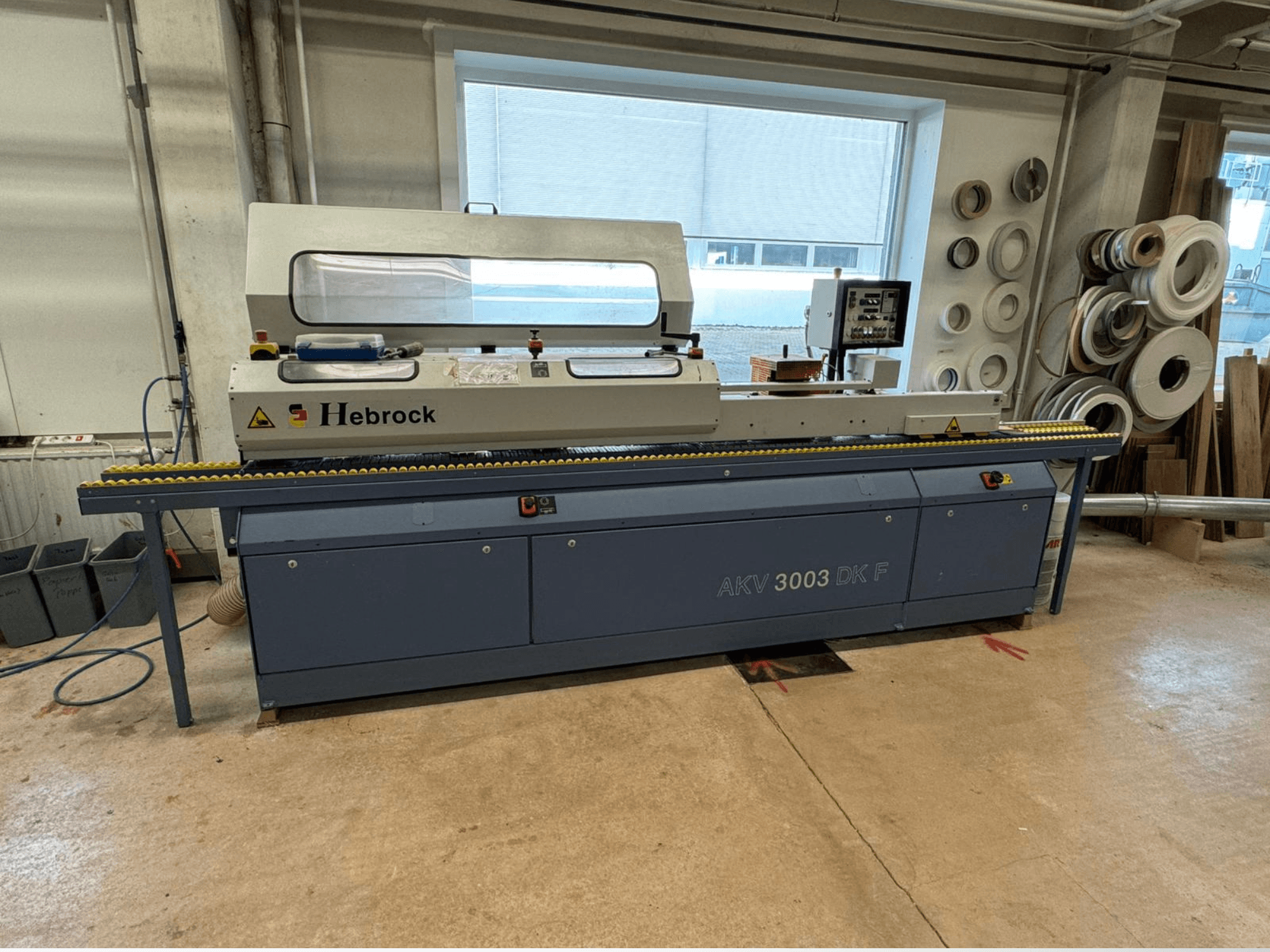 Hebrock AKV 3003 DK F kantenaanlijmmachine, vooraanzicht, voorzien van een transportband en bedieningspaneel, opgesteld in een werkplaats.