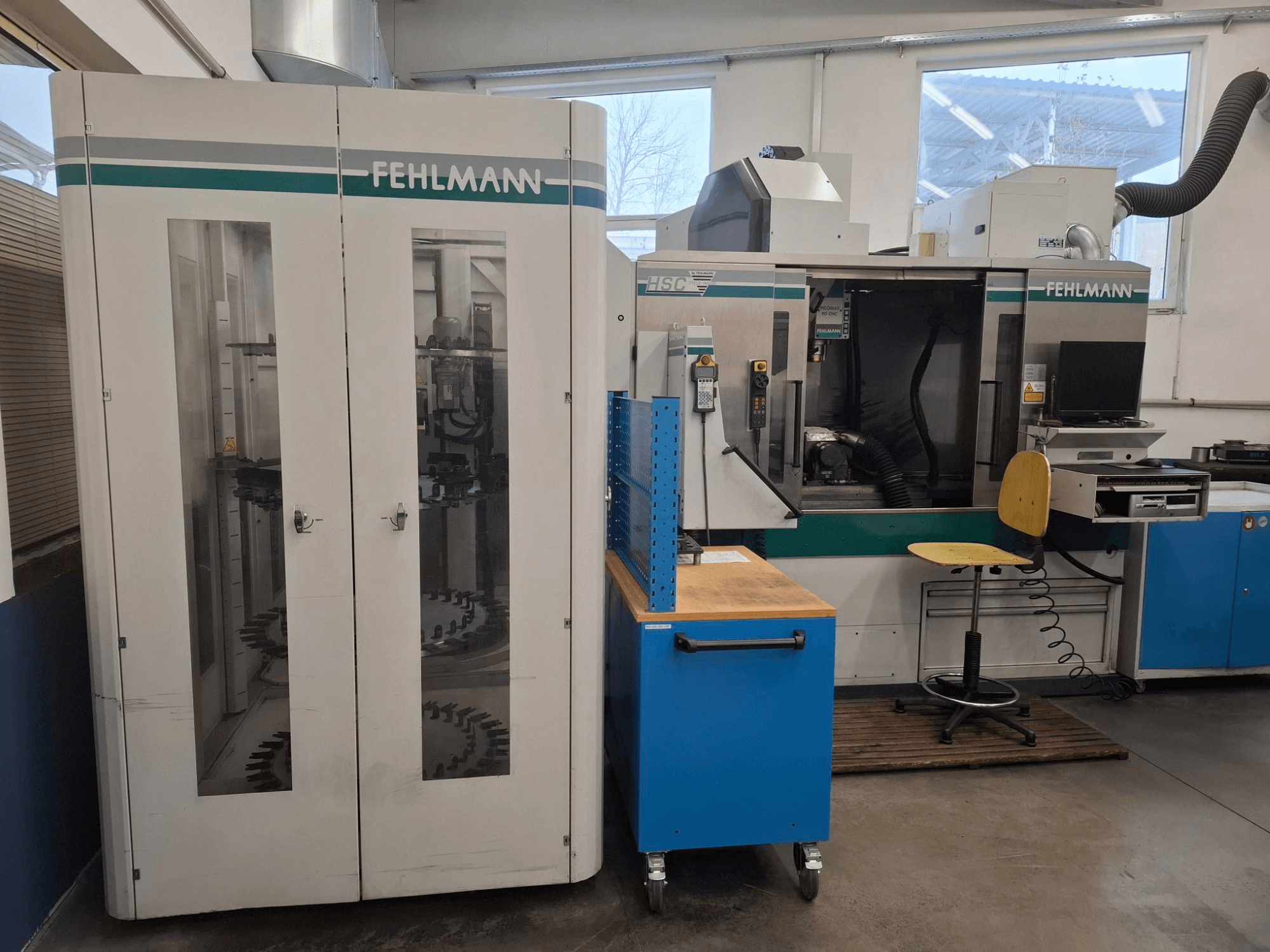 FEHLMANN HSC bewerkingscentrum in een werkplaats; vooraanzicht met zichtbare bedieningselementen, stoelen en gereedschapopslag.