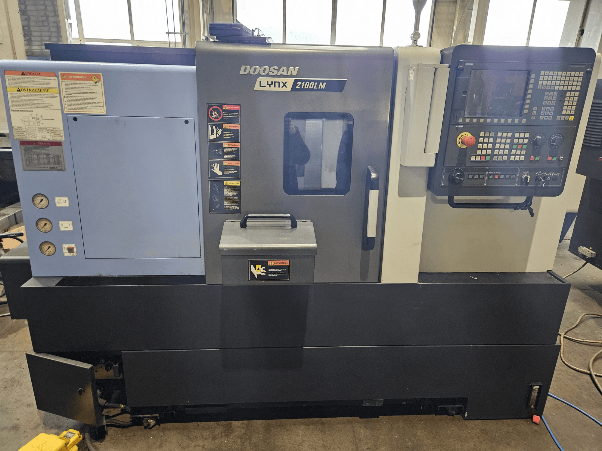 Doosan Lynx 2100LM CNC draaibank, vooraanzicht, met bedieningspaneel, luchtdrukmeters en veiligheidslabels zichtbaar.