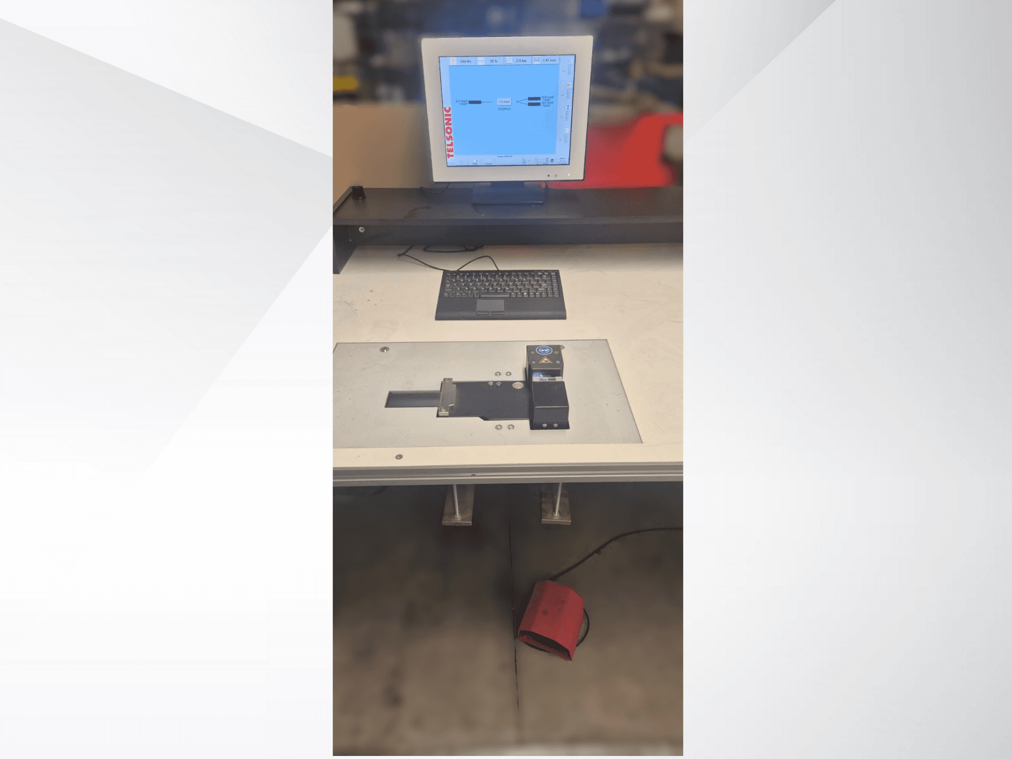 Een bovenaanzicht van een teststation met een computermonitor, toetsenbord en bedieningspaneel met een knop en een groen lampje.