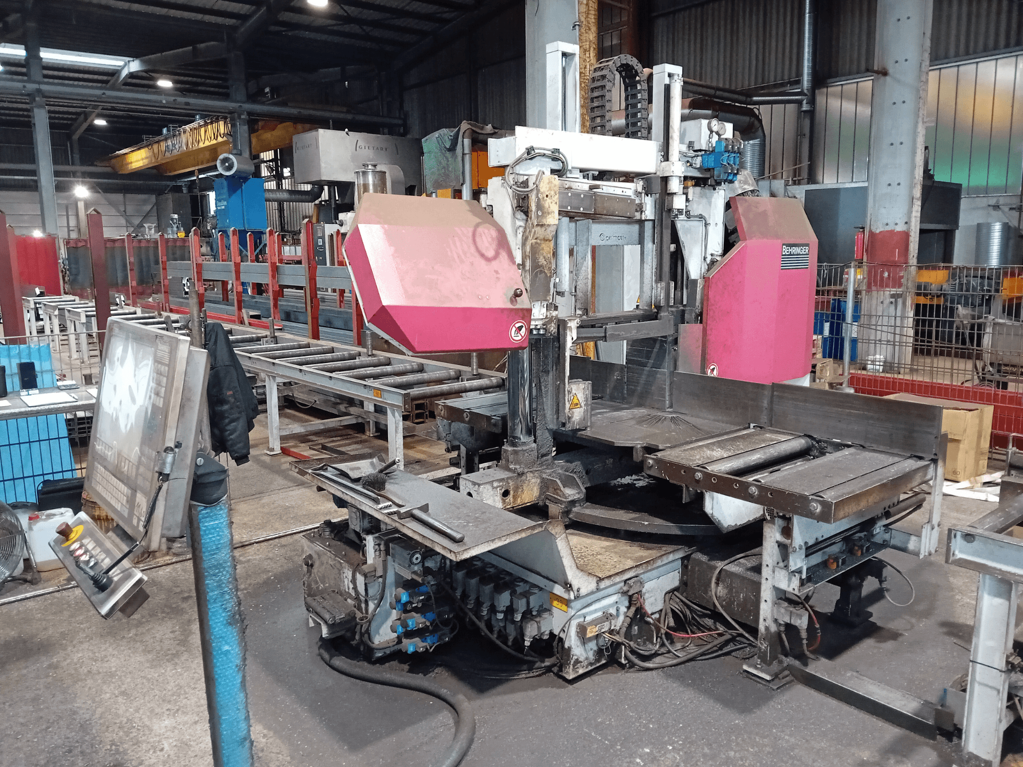 Behringer lintzaagmachine in een fabriek, vooraanzicht, met een groot zaagblad en bedieningspaneel met knoppen.