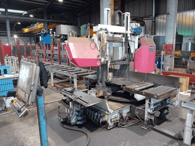Behringer lintzaagmachine in een fabriek, vooraanzicht, met een groot zaagblad en bedieningspaneel met knoppen.