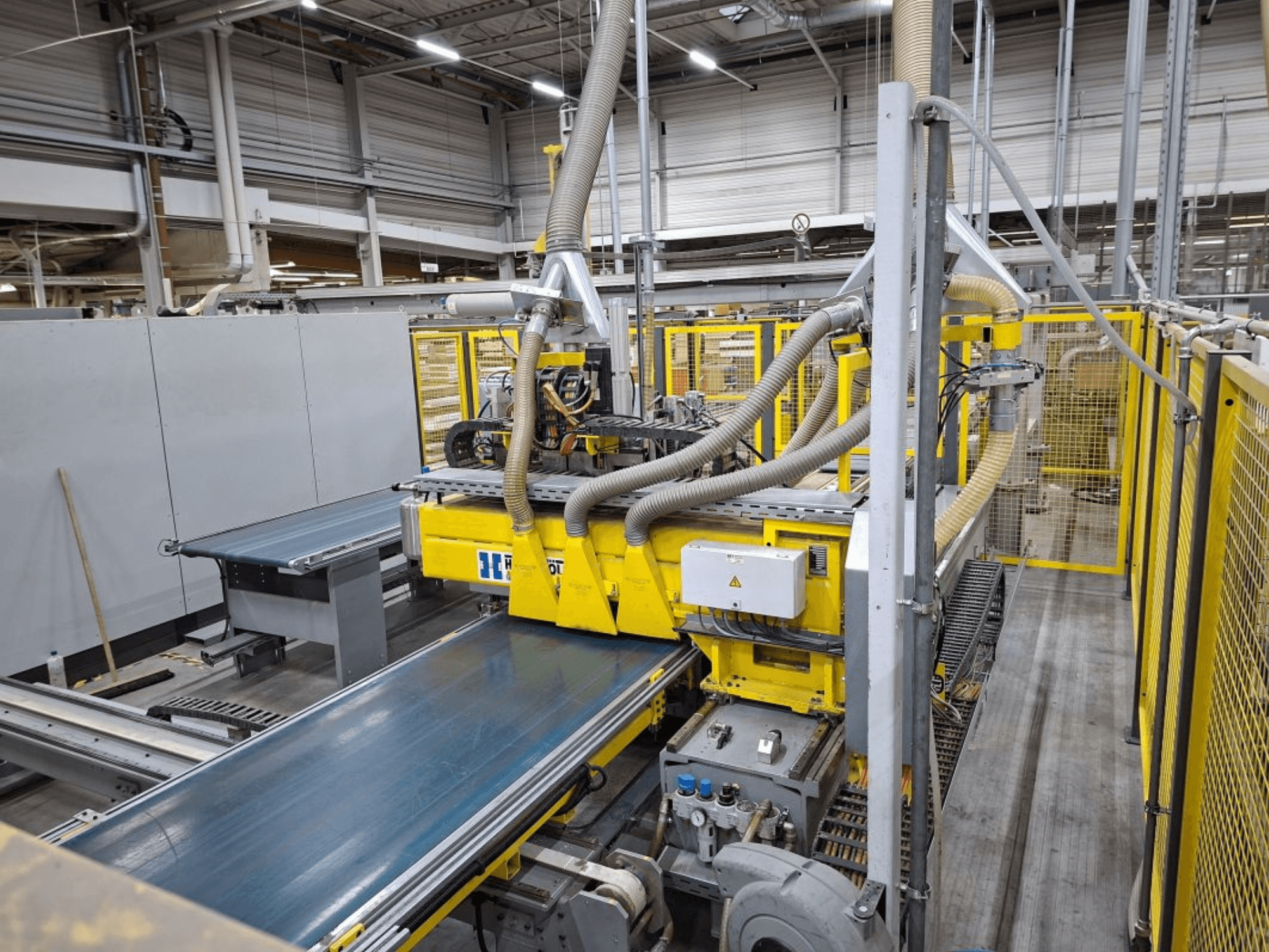 Industrieel transportsysteem vanuit zijaanzicht, met gele machines, bedieningspaneel en slangaansluitingen voor productie.