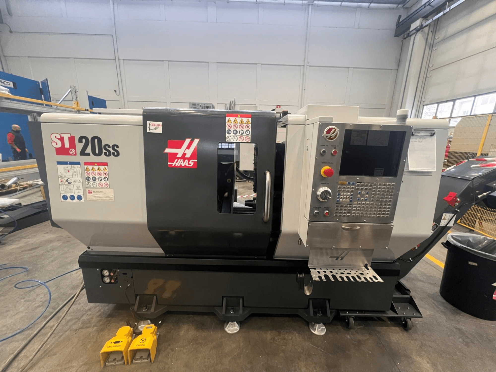 Haas ST 20SS CNC draaibank in zijaanzicht, met bedieningspaneel, veiligheidslabels en voetpedalen op de vloer.