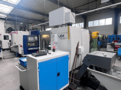Industriële werkplaats met een Heller bewerkingscentrum, vooraanzicht met gereedschap, bedieningselementen en omringende apparatuur.