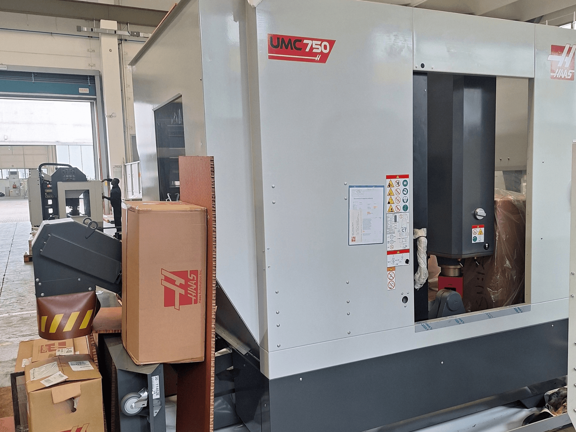 HAAS UMC-750 universeel bewerkingscentrum, zijaanzicht, met het bedieningspaneel en de gereedschapopslag met waarschuwingslabels en verpakking.