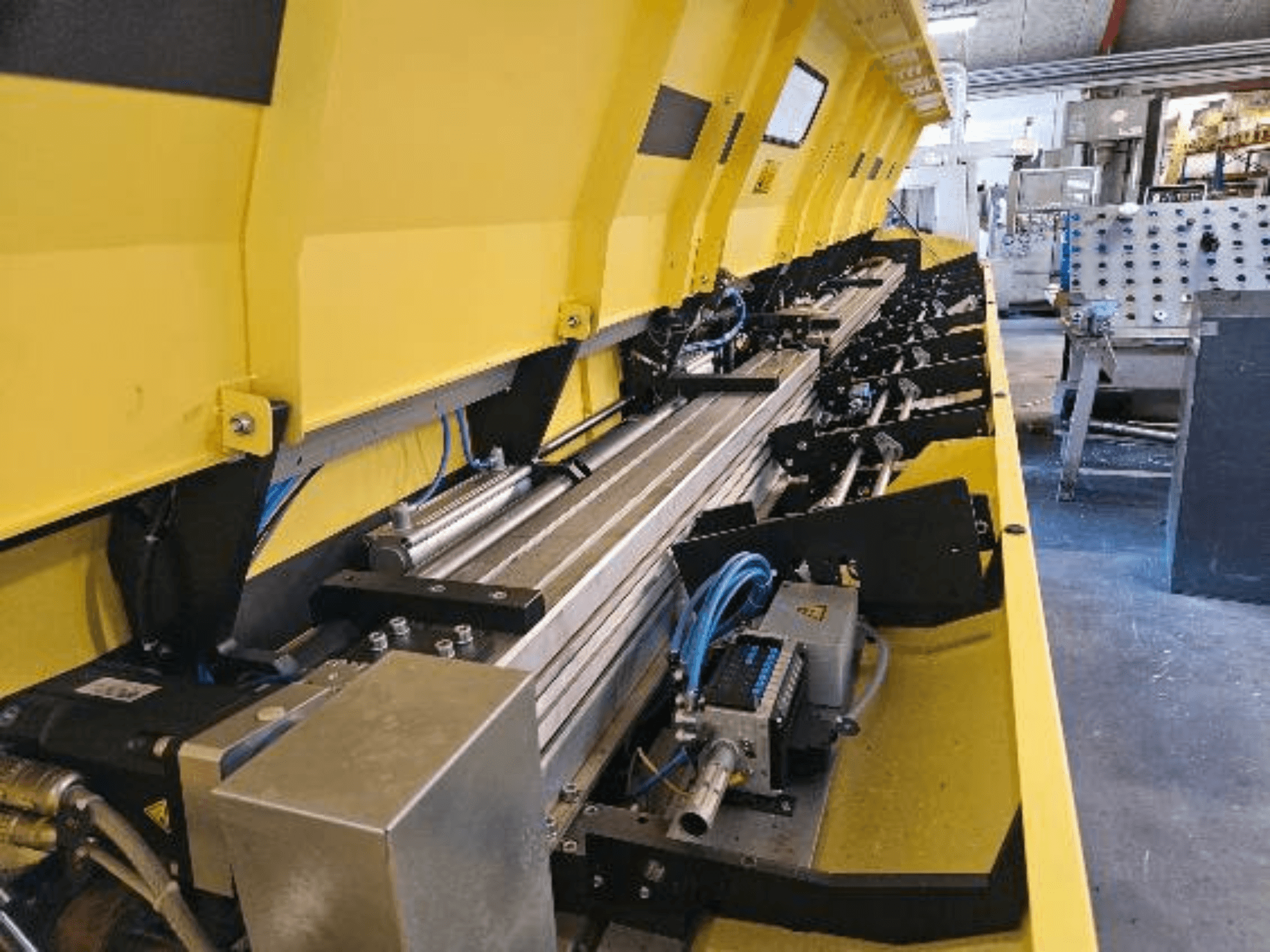 Close-up van een gele hydraulische machine met metalen onderdelen en transportbanden, met slangen en elektronische onderdelen.