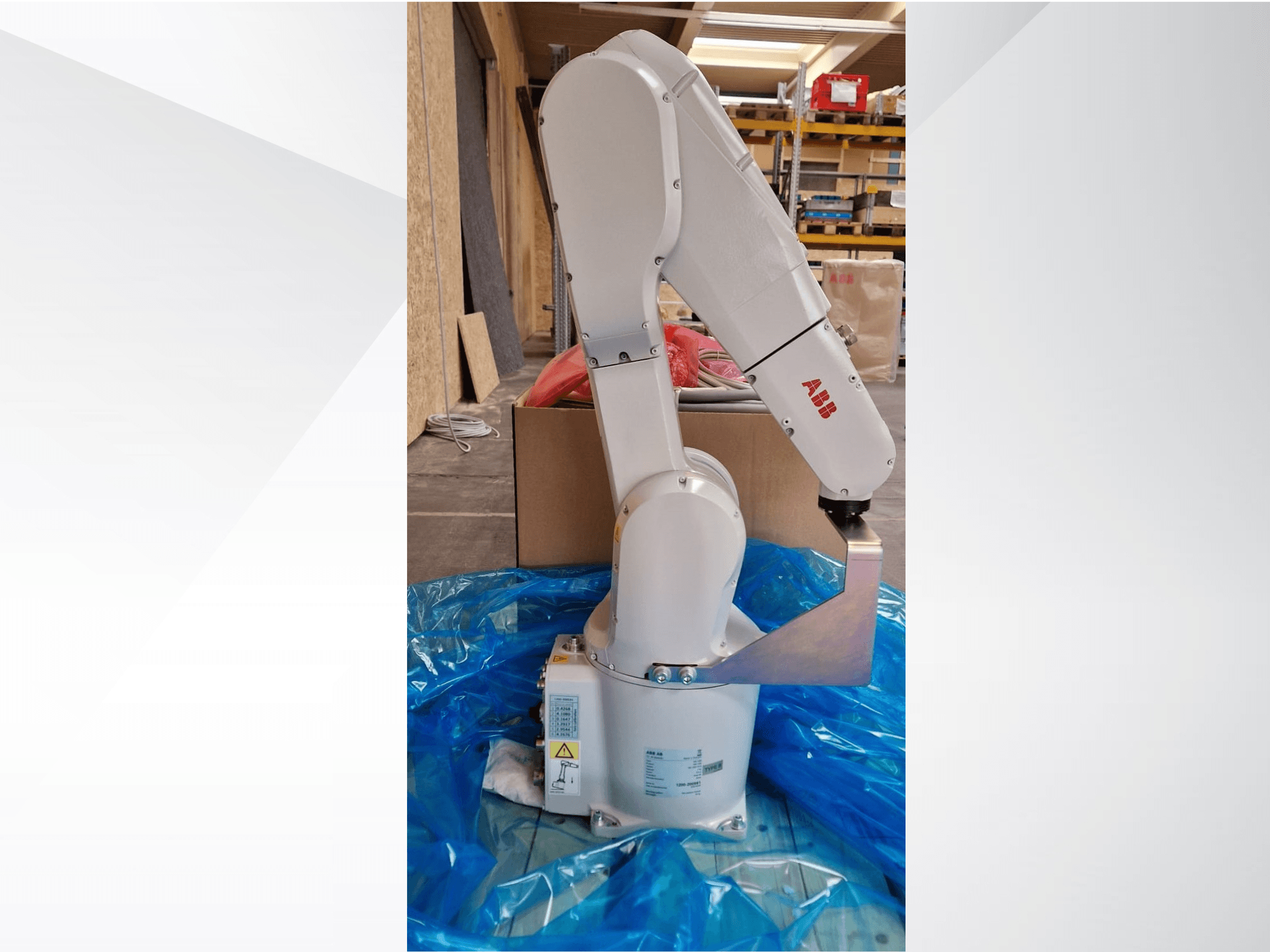 ABB robotarm model, zijaanzicht op blauw zeil, met de scharnierende gewrichten en metalen eindeffector, met technische labels zichtbaar.