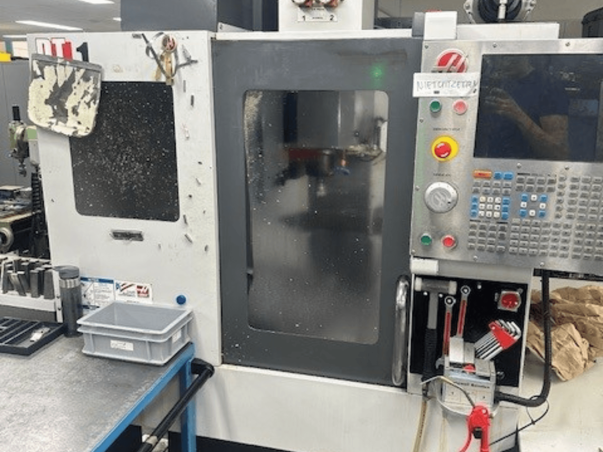 Haas DT-1 verticaal bewerkingscentrum, vooraanzicht met bedieningspaneel, zichtbaar vuil en gereedschapsbak op de werkbank.
