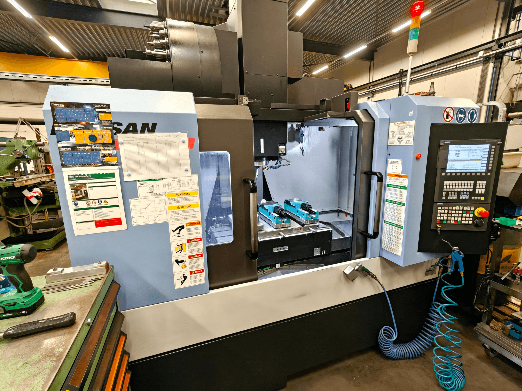 DOOSAN DNM 400 II verticaal bewerkingscentrum in een werkplaats, met bedieningselementen, gereedschapshouders en veiligheidsborden, vooraanzicht.