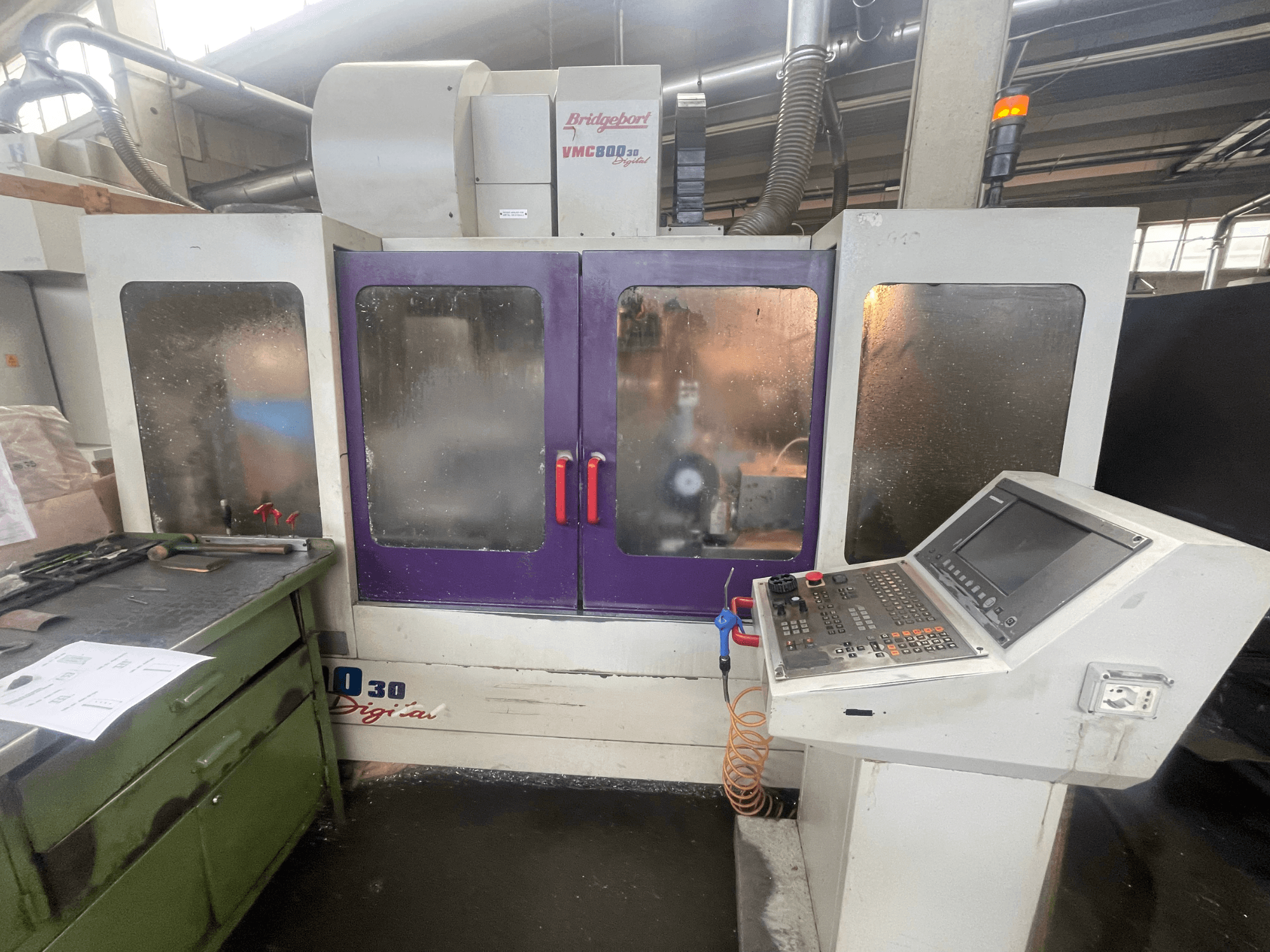 Bridgeport VMC 800/30 verticaal bewerkingscentrum, vooraanzicht, met het bedieningspaneel en de paarse deuren, gereedschap op het aangrenzende oppervlak.