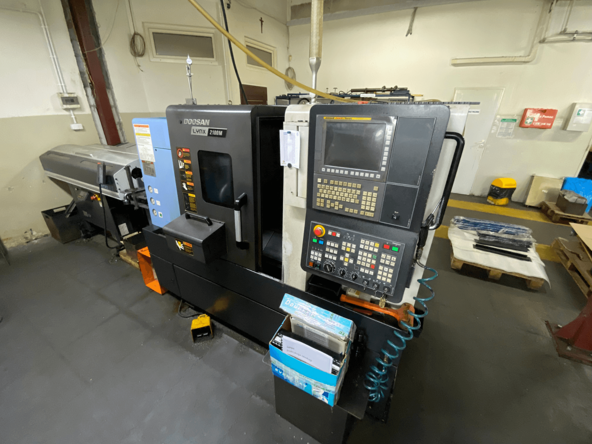 De DOOSAN LYNX 2100MA horizontale draaimachine, gezien vanaf de zijkant, met bedieningspaneel, gereedschap en werkgebied.