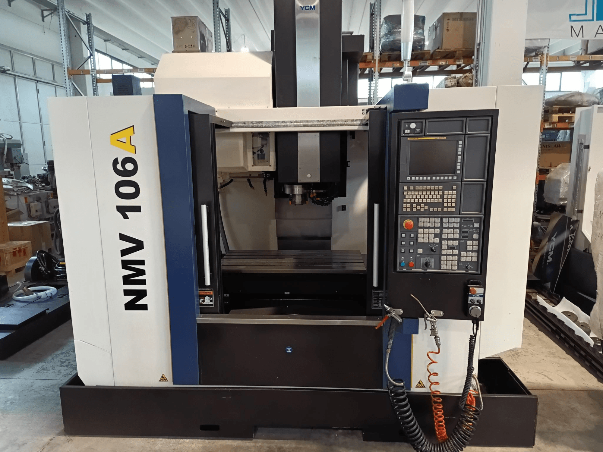 YCM NMV 106A bewerkingscentrum, vooraanzicht, met bedieningspaneel met knoppen en koelvloeistofslangen.