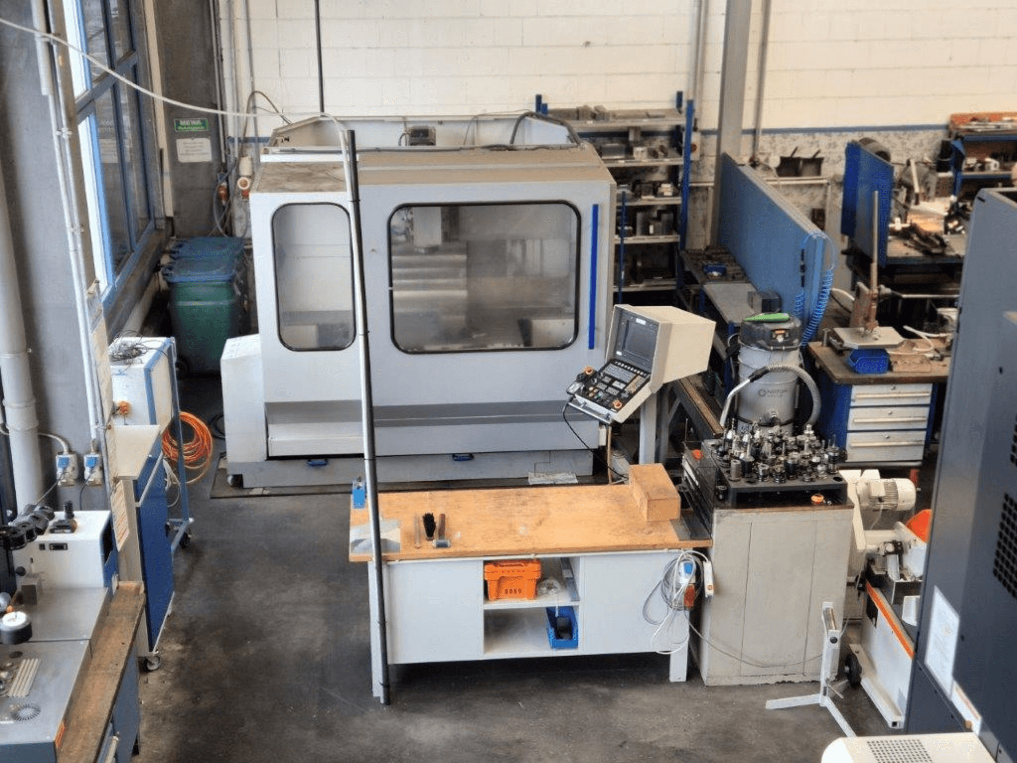 CNC freesmachine in een werkplaats, vooraanzicht, met bedieningspaneel, werkoppervlak en gereedschappen zichtbaar op de achtergrond.