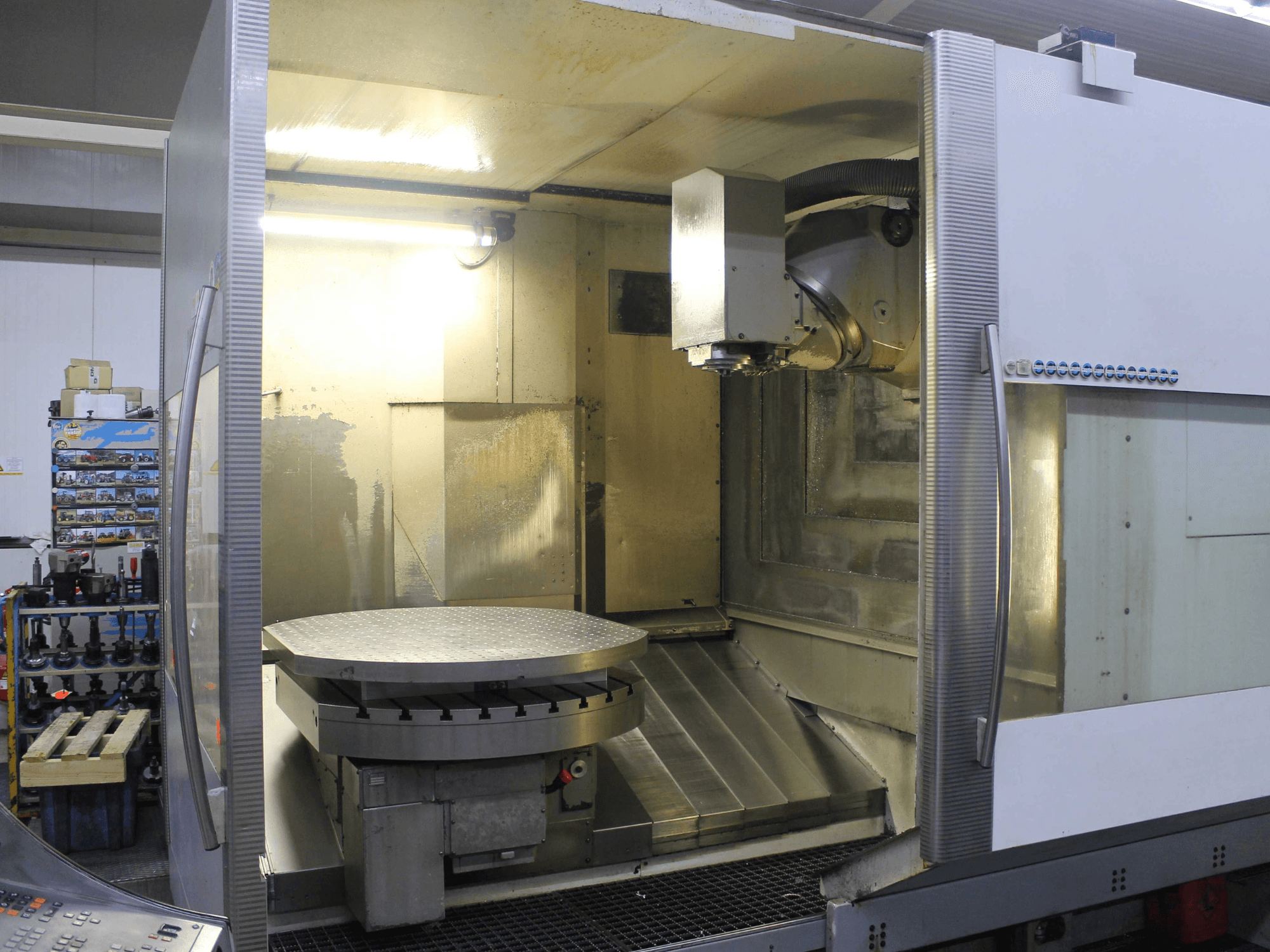 CNC freesmachine met ronde draaitafel en snijkop, vooraanzicht, met metalen oppervlakken en verlichting.