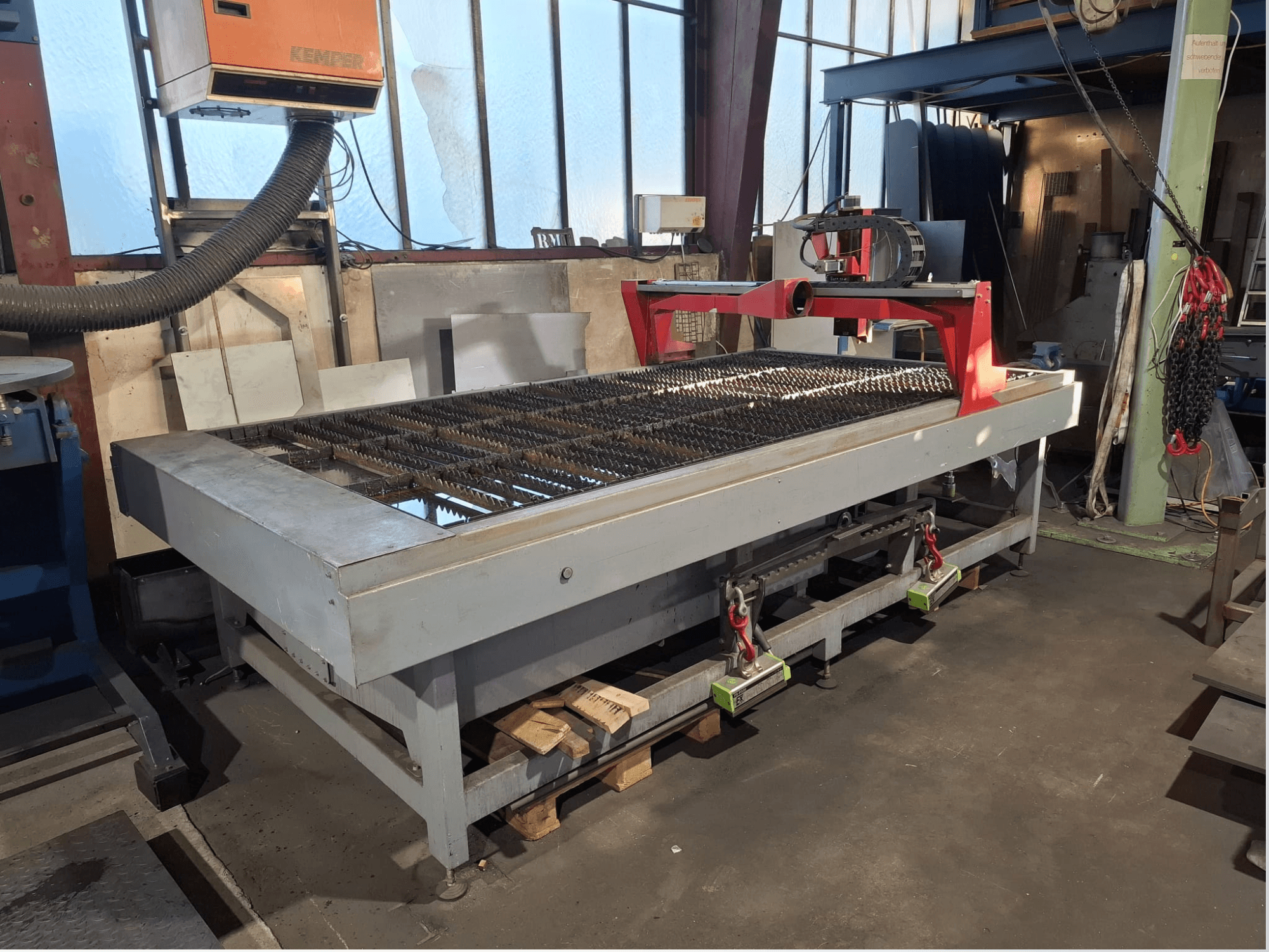De PLASMACUT 3015T-plasmasnijmachine, afgebeeld in zijaanzicht, met een grote snijtafel met metalen latten en een rood frame.