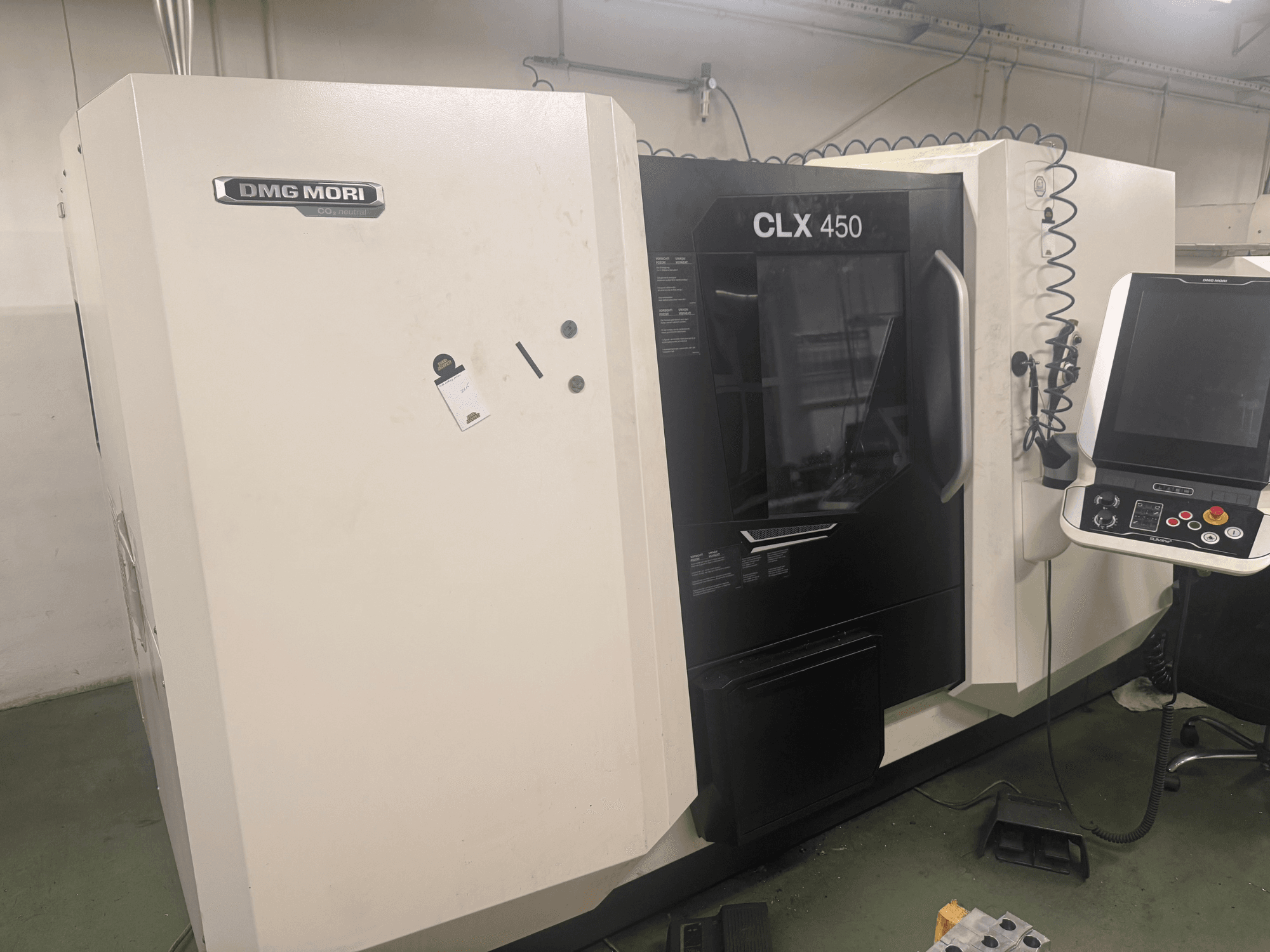 DMG MORI CLX 450 CNC machine, zijaanzicht met bedieningspaneel, zichtbare bedieningsknoppen en schone werkruimte.