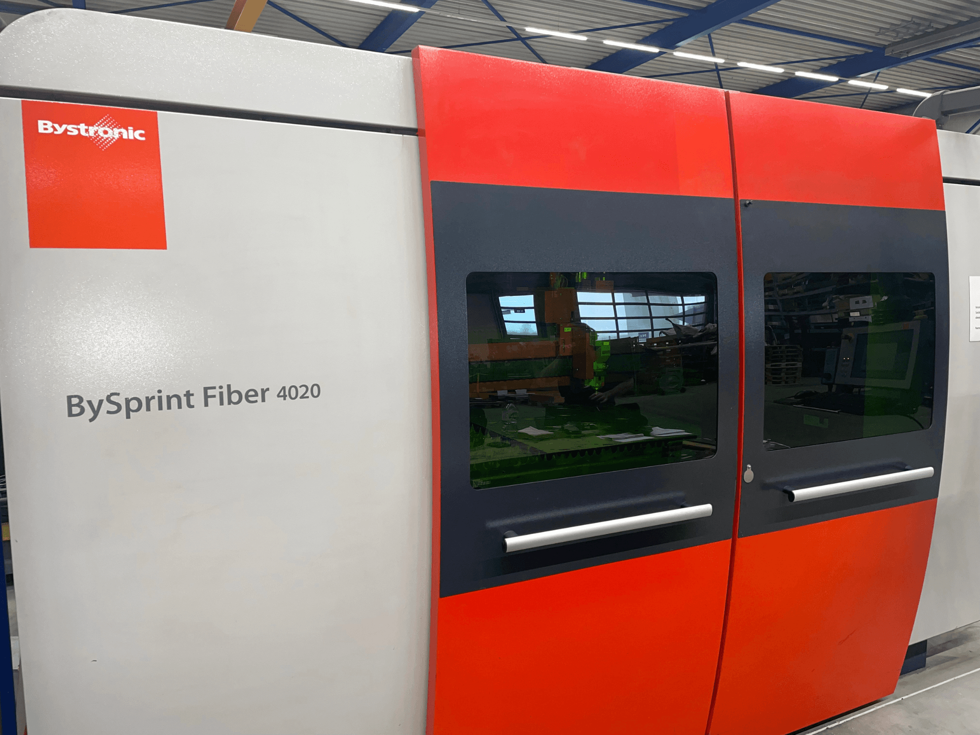Bystronic BySprint Fiber 4020 in vooraanzicht, met een grijs en rood paneelontwerp met grote vensters en bedieningsinterface zichtbaar binnenin.