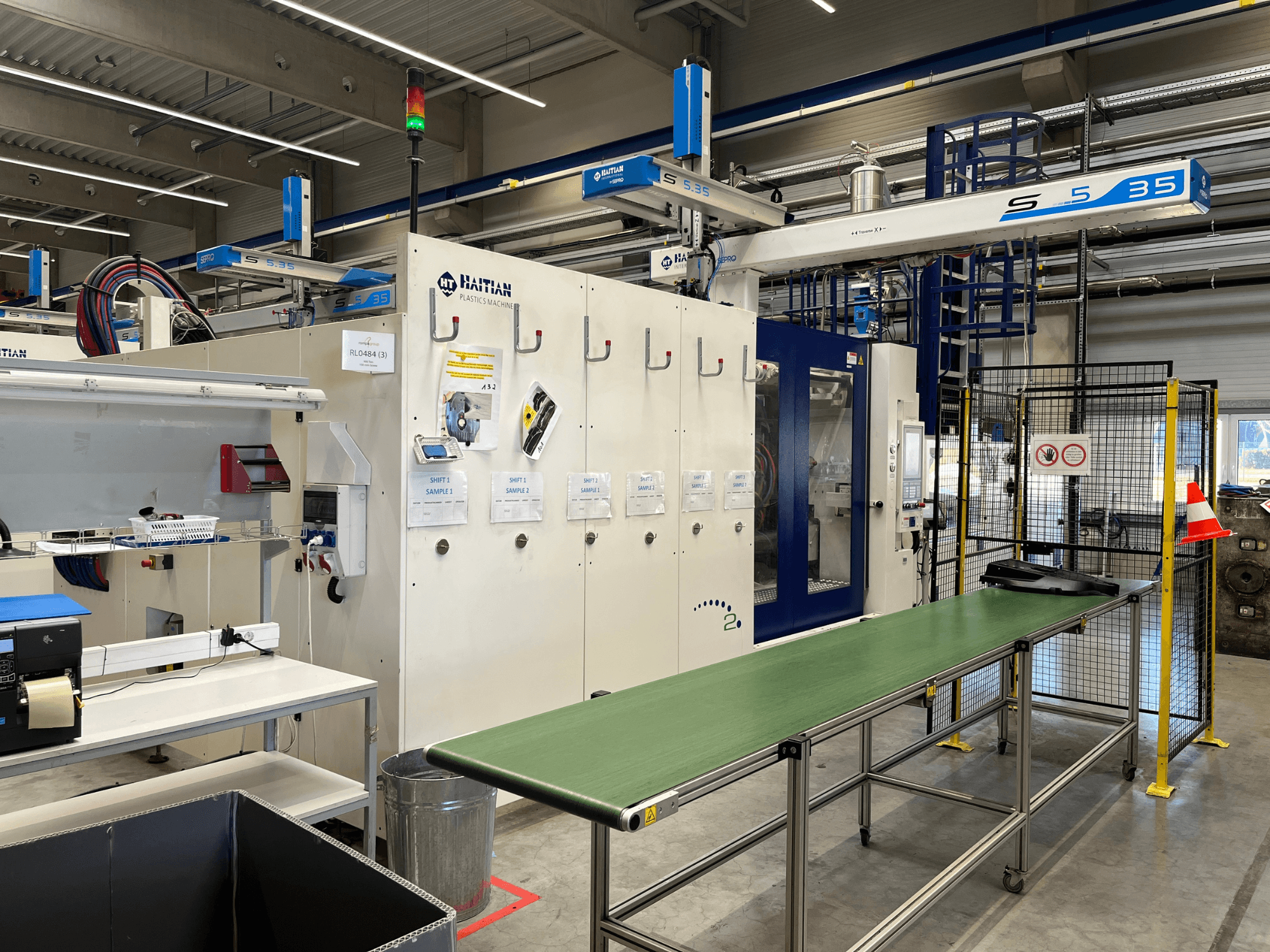 Haïtiaanse S5-35 kunststofmachine in een werkplaats; groene transportband, veiligheidshekken en bedieningspaneel zichtbaar in vooraanzicht.