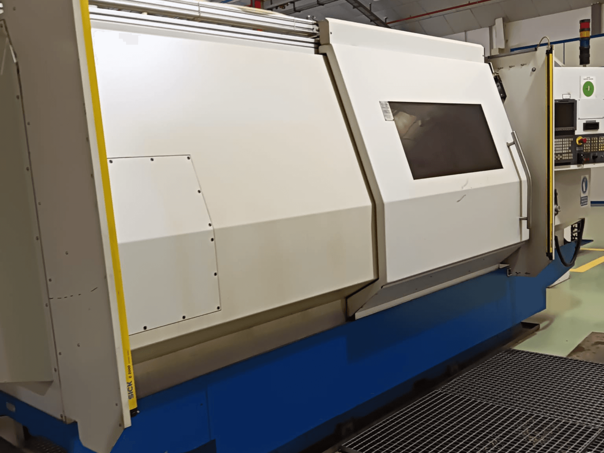 Industriële draaibank, zijaanzicht, met een grote witte en blauwe behuizing, digitaal bedieningspaneel en veiligheidsfuncties.