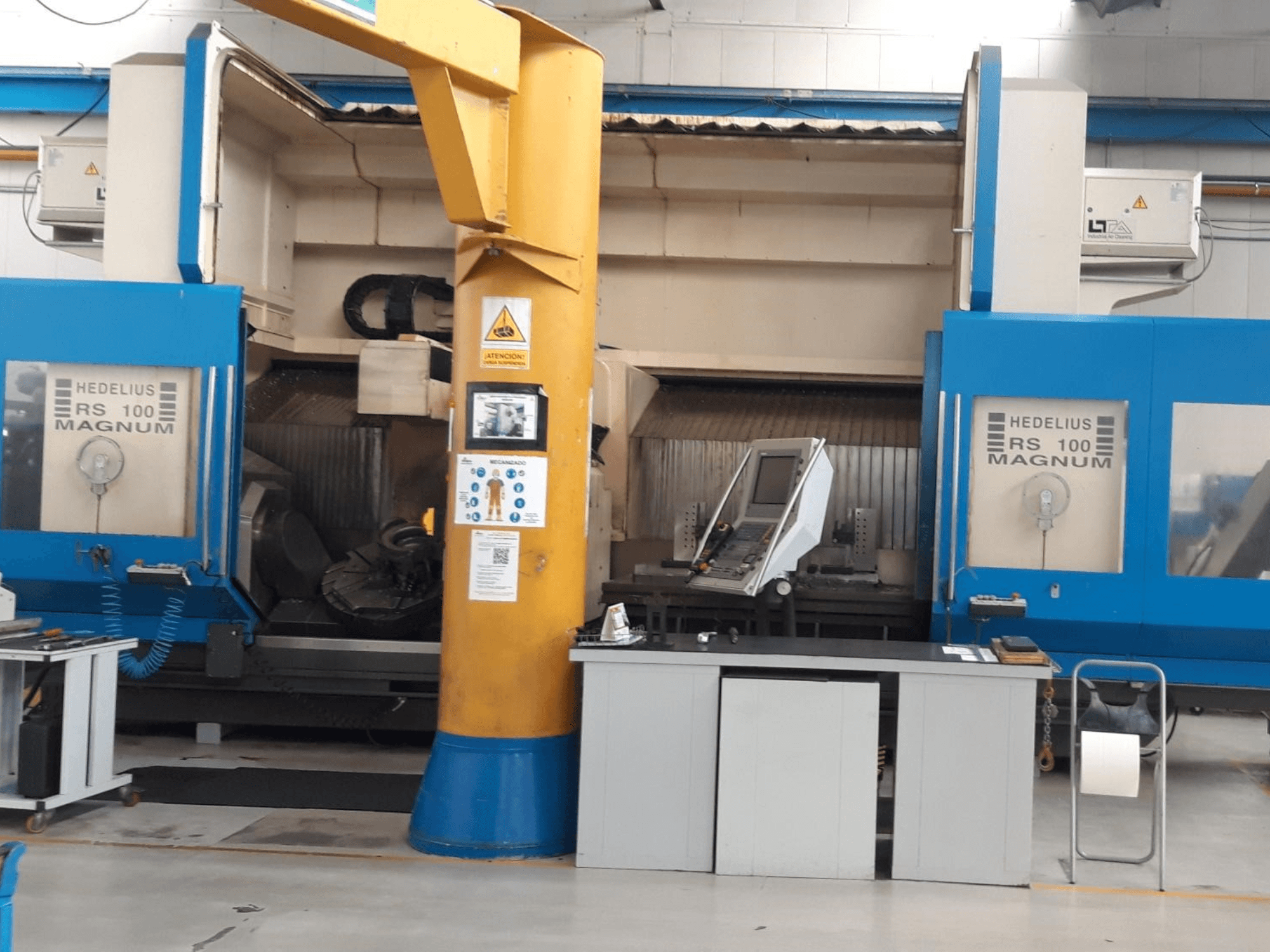 HEDALIUS RS 100 MAGNUM machine, vooraanzicht; voorzien van bedieningspaneel en gele steunkolom, opgesteld in een industriële werkruimte.