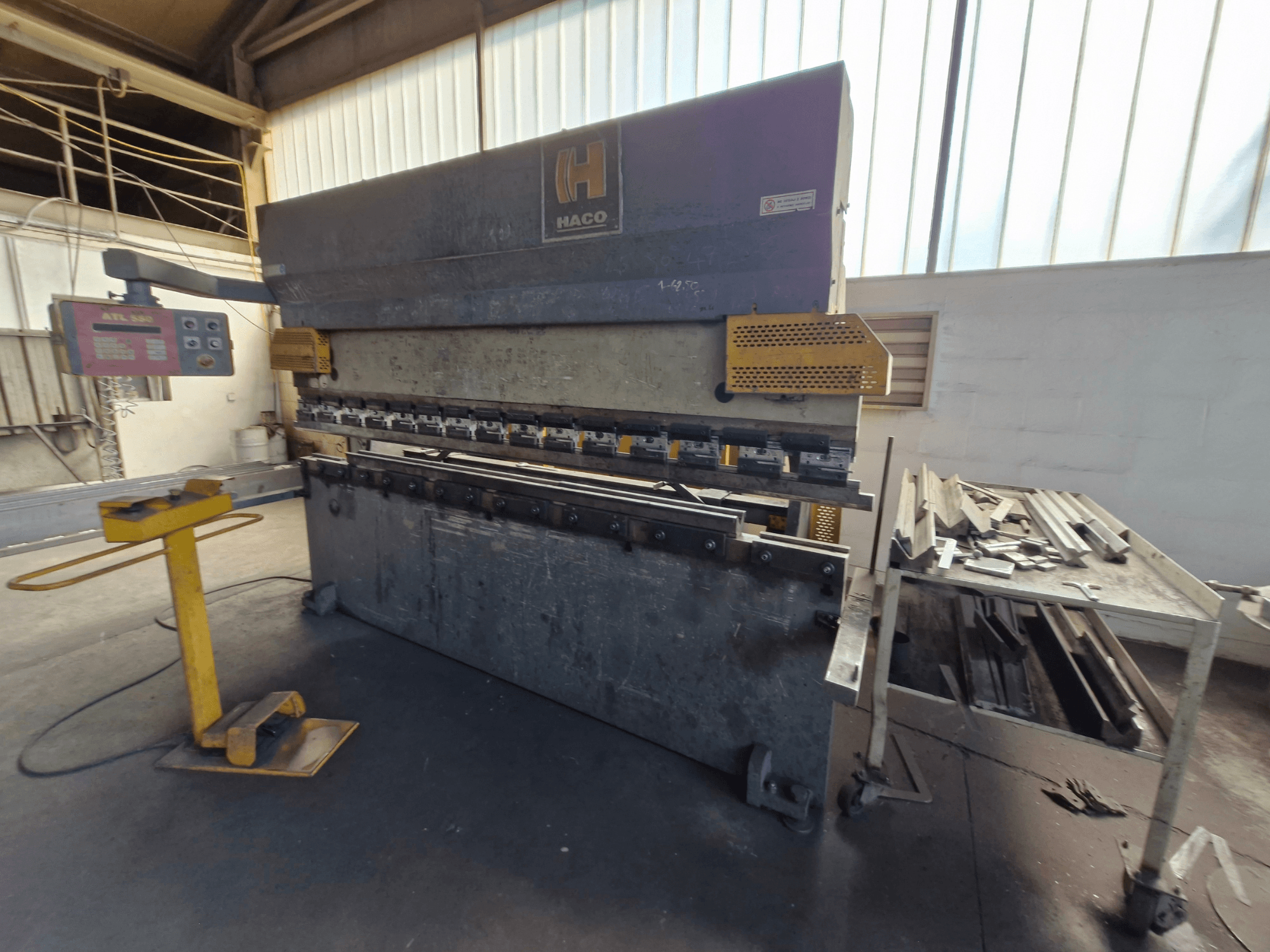 HACO PPM 30135 b kantpers in een werkplaats, vooraanzicht met bedieningspaneel en schroot op een tafel ernaast.