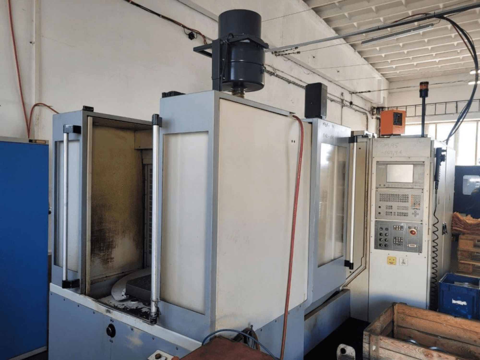 Industriële CNC freesmachine met bedieningspaneel, zijaanzicht, toont behuizing en zichtbaar vuil op oppervlakken.