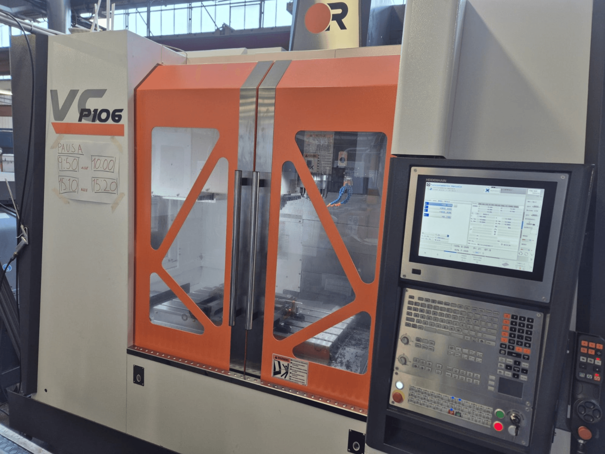 Alt-tekst: Oranje en grijze VF P106 CNC machine, vooraanzicht, met een bedieningspaneel en geplande bewerkingstijden op papier.