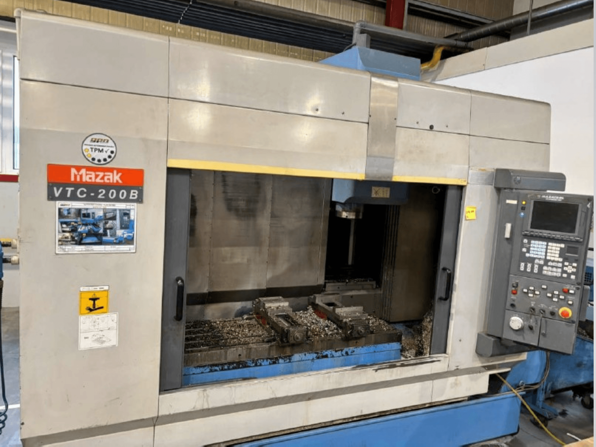 Mazak VTC-200B verticaal bewerkingscentrum, zijaanzicht met zichtbaar bedieningspaneel en metaalschilfers in het werkgebied.