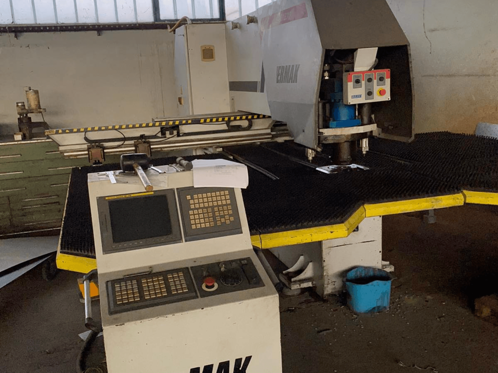 Ermak CNC machine, vooraanzicht, met bedieningspaneel, snijkop op een rubberen mat en nabijgelegen gereedschap in een industriële omgeving.