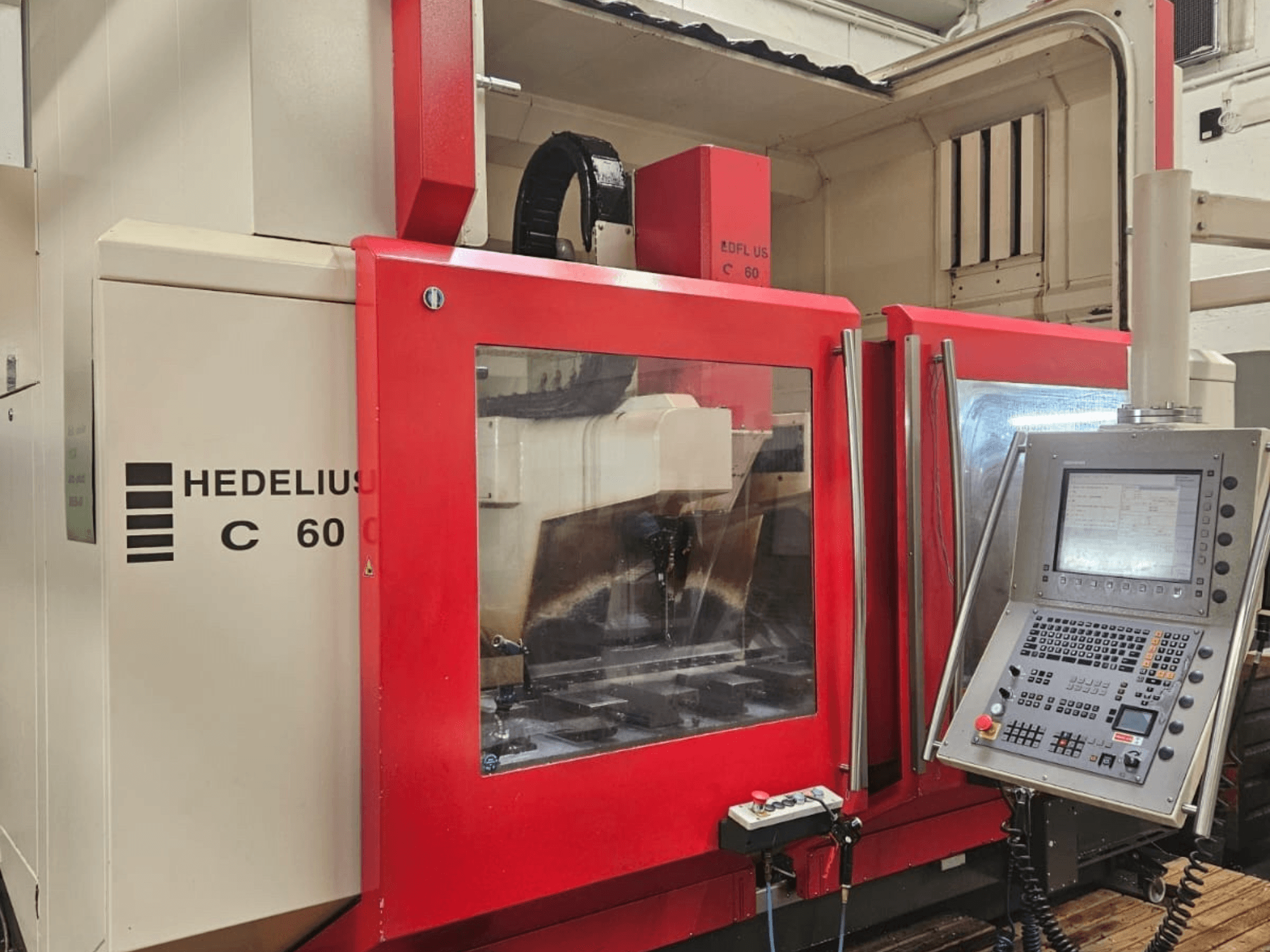 HEDELIUS C60 verticaal bewerkingscentrum vanaf de zijkant, met een rood voorpaneel en bedieningsconsole met display.