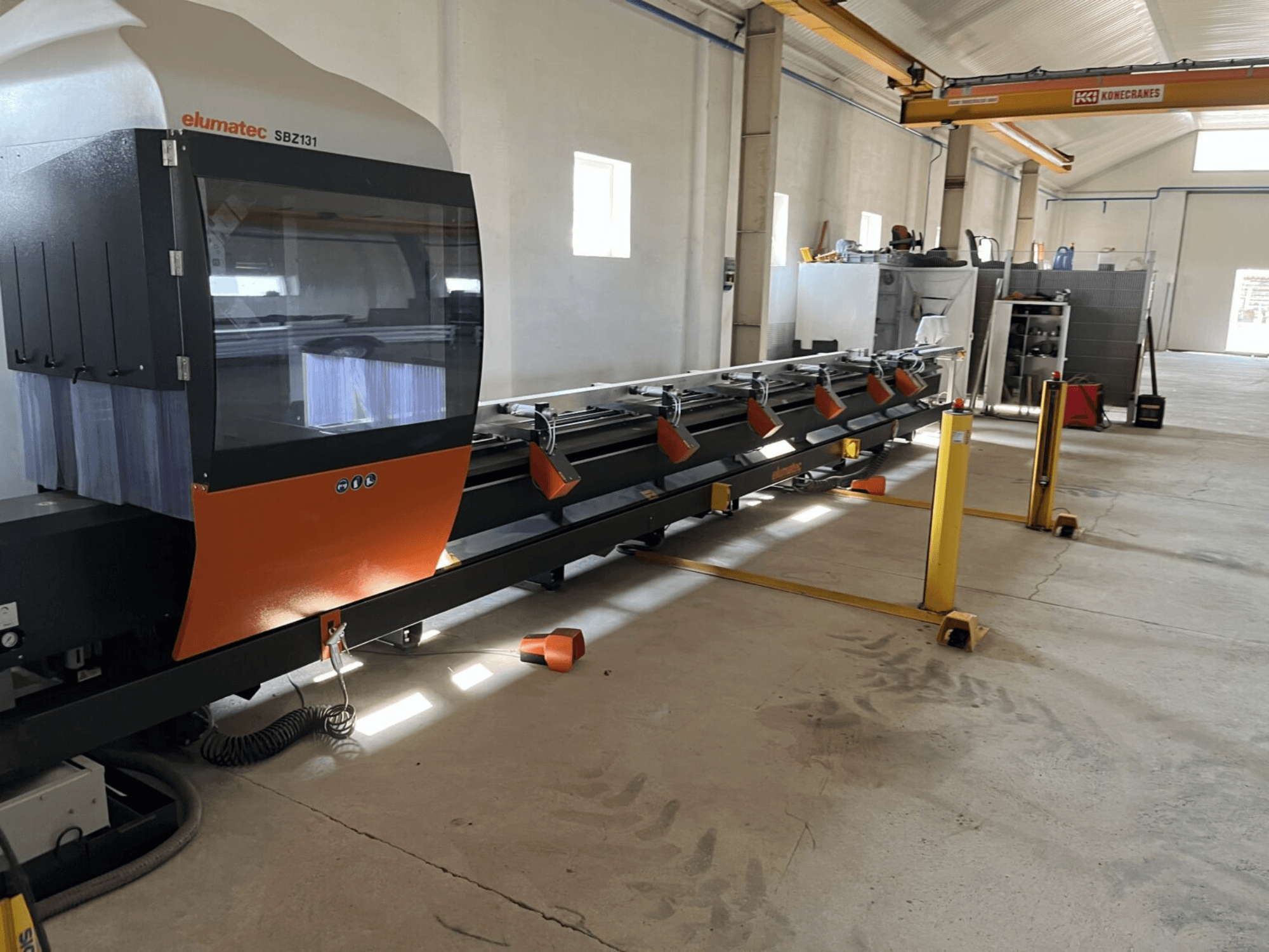 Elumatec SBZ131, vooraanzicht van een lineaire freesmachine met oranje en zwart design, in een werkplaatsomgeving.