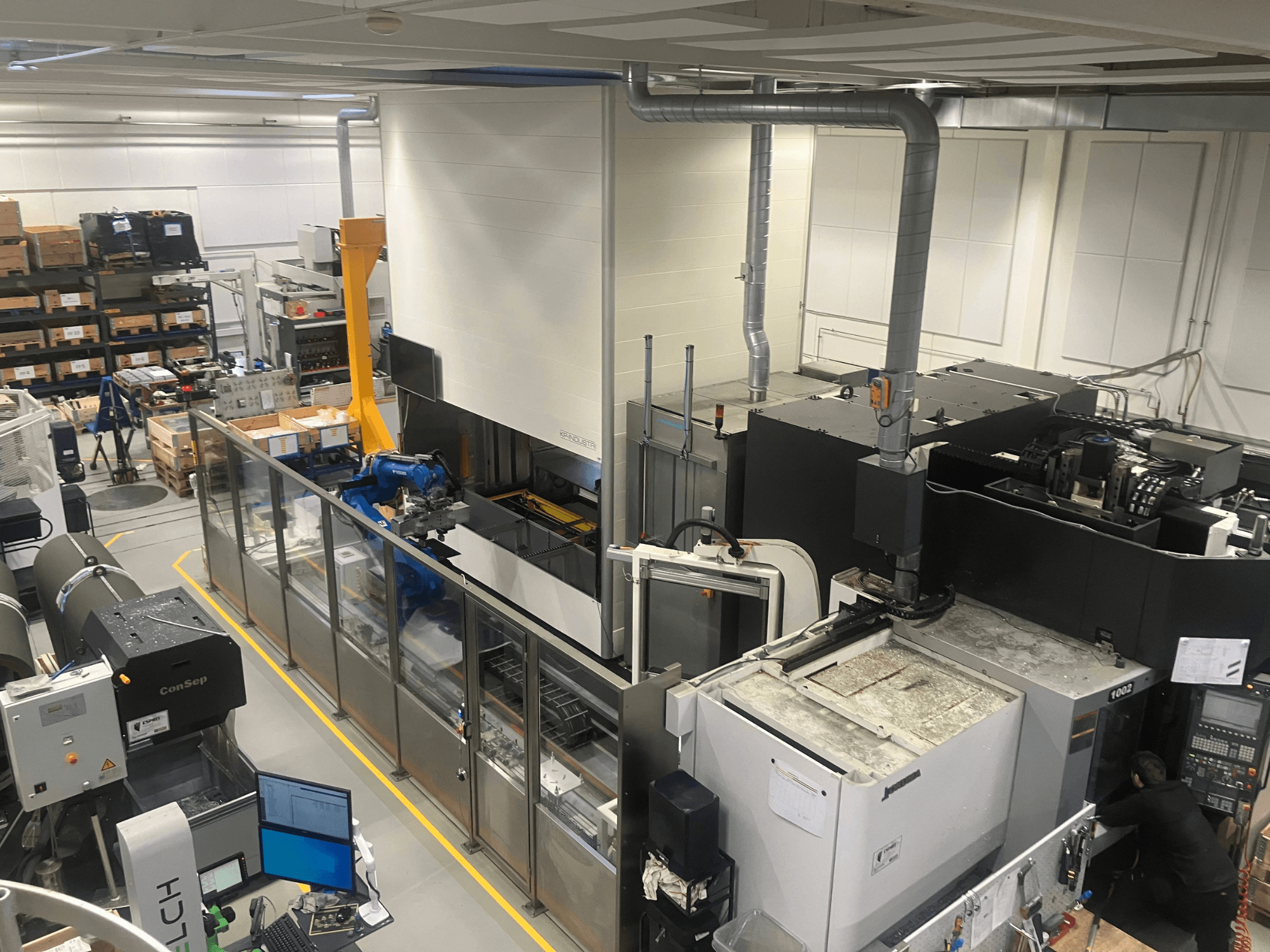 SSI SCHAFER Logimat automatiseringssysteem in een magazijn, vooraanzicht; voorzien van robotarm, opslagrekken en machines.