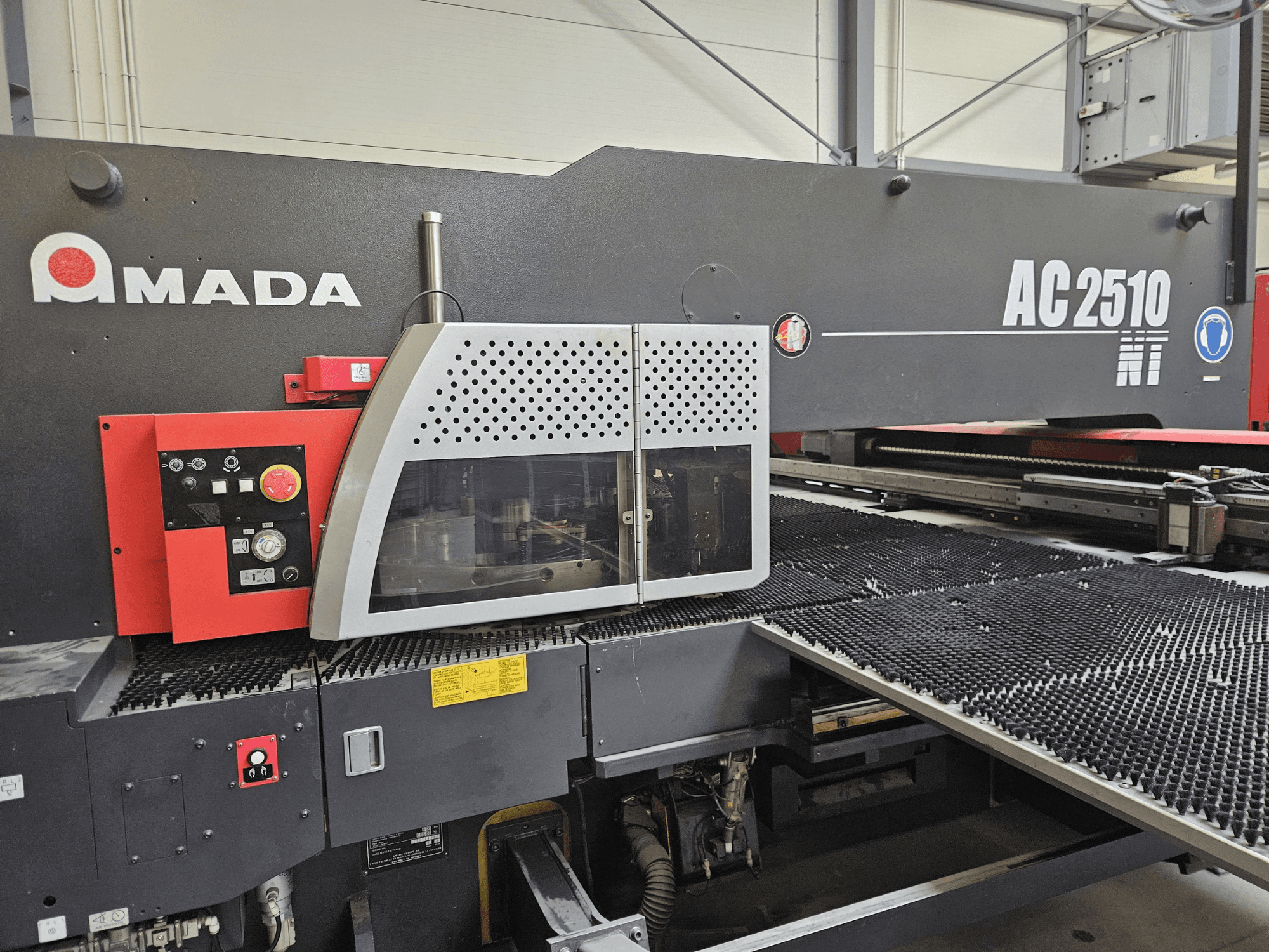 Amada AC2510 NT lasersnijmachine, vooraanzicht, met bedieningspaneel met knoppen en een veiligheidskap.