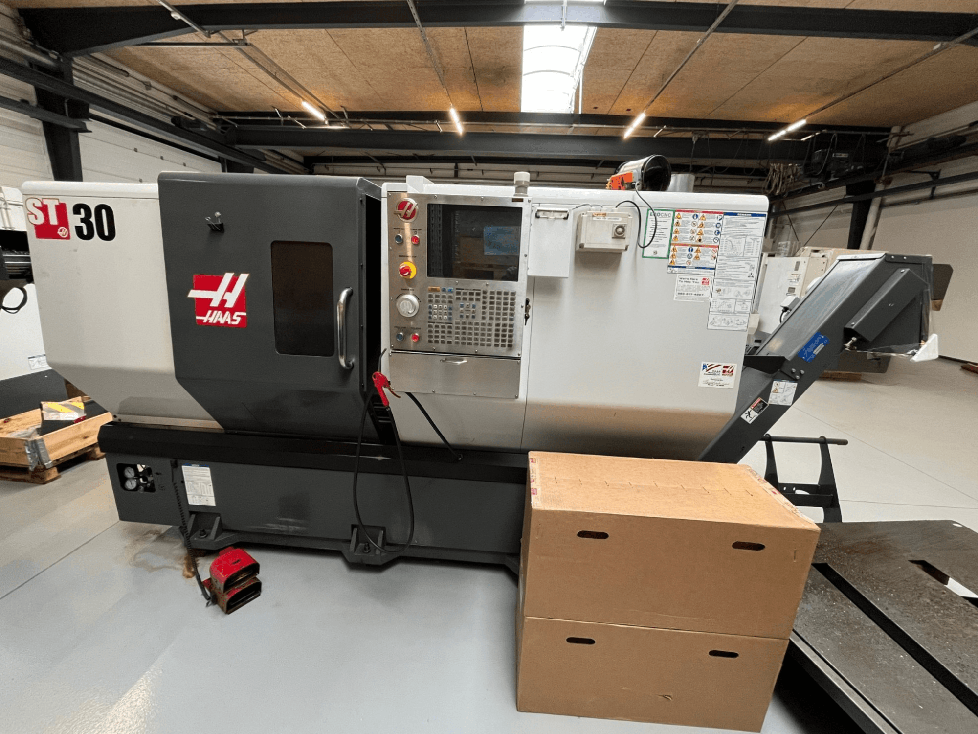 Haas ST-30 CNC draaibank, vooraanzicht, met bedieningspaneel met knoppen, noodstop en twee gestapelde kartonnen dozen.