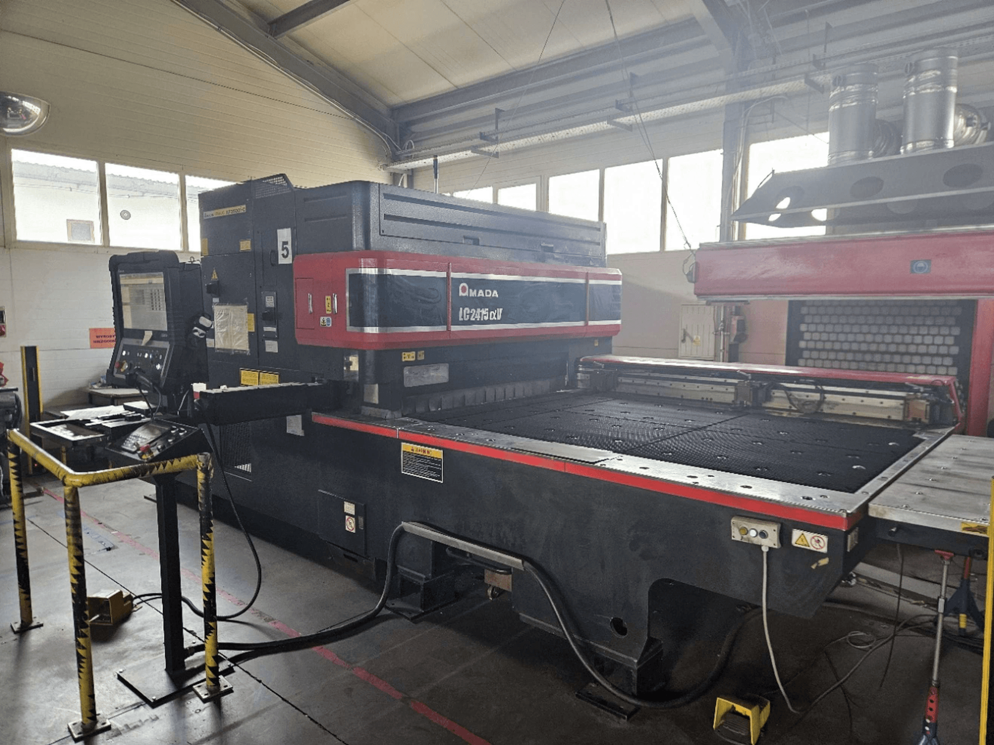 AMADA LC2415 Alpha 5 CO₂-lasersnijmachine, vooraanzicht met bedieningspaneel en snijtafel met veiligheidshekken.