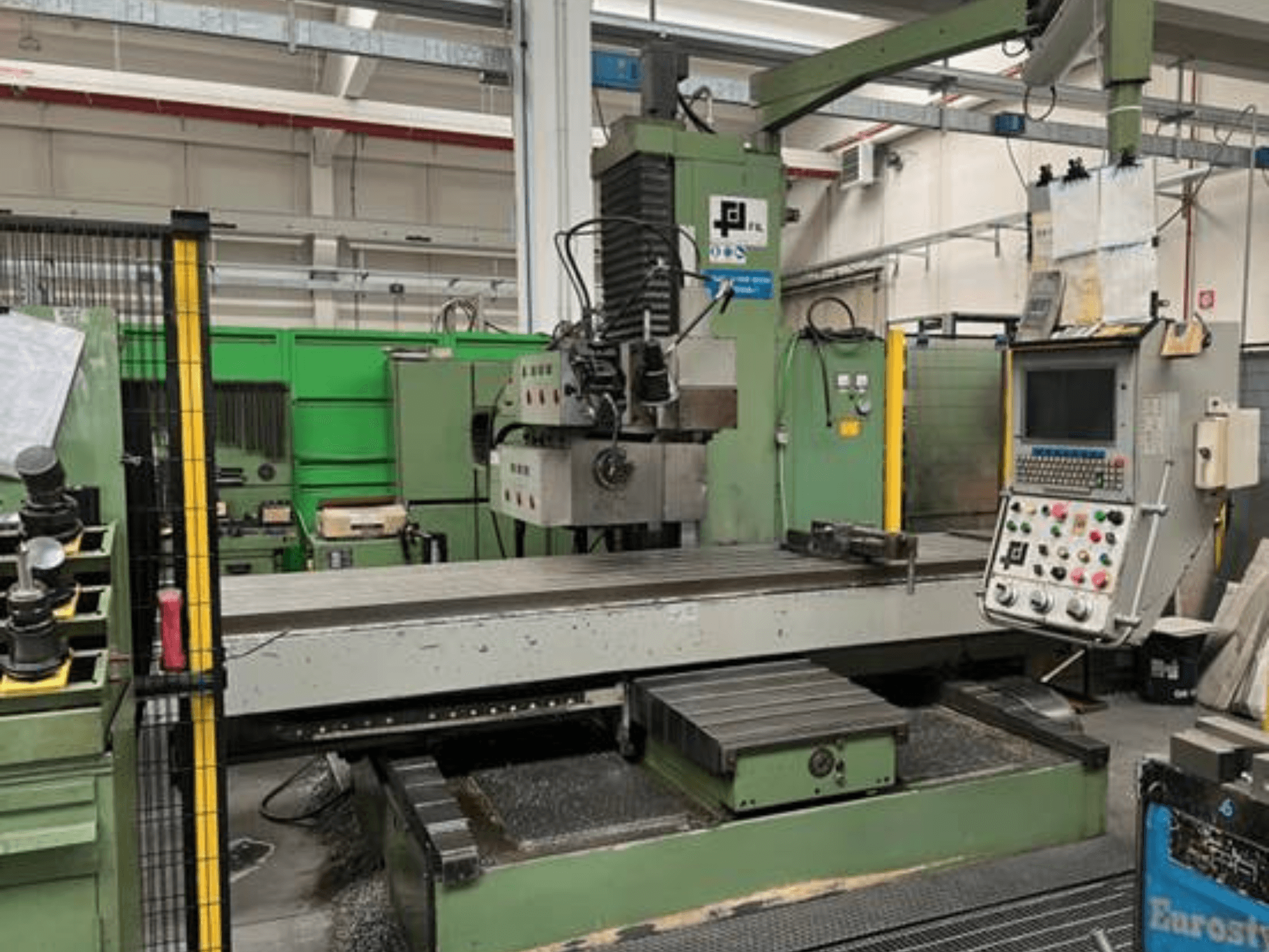 Industriële freesmachine van JFL, vooraanzicht met bedieningspaneel, grote vlakke tafel en metaalschilfers op de vloer.