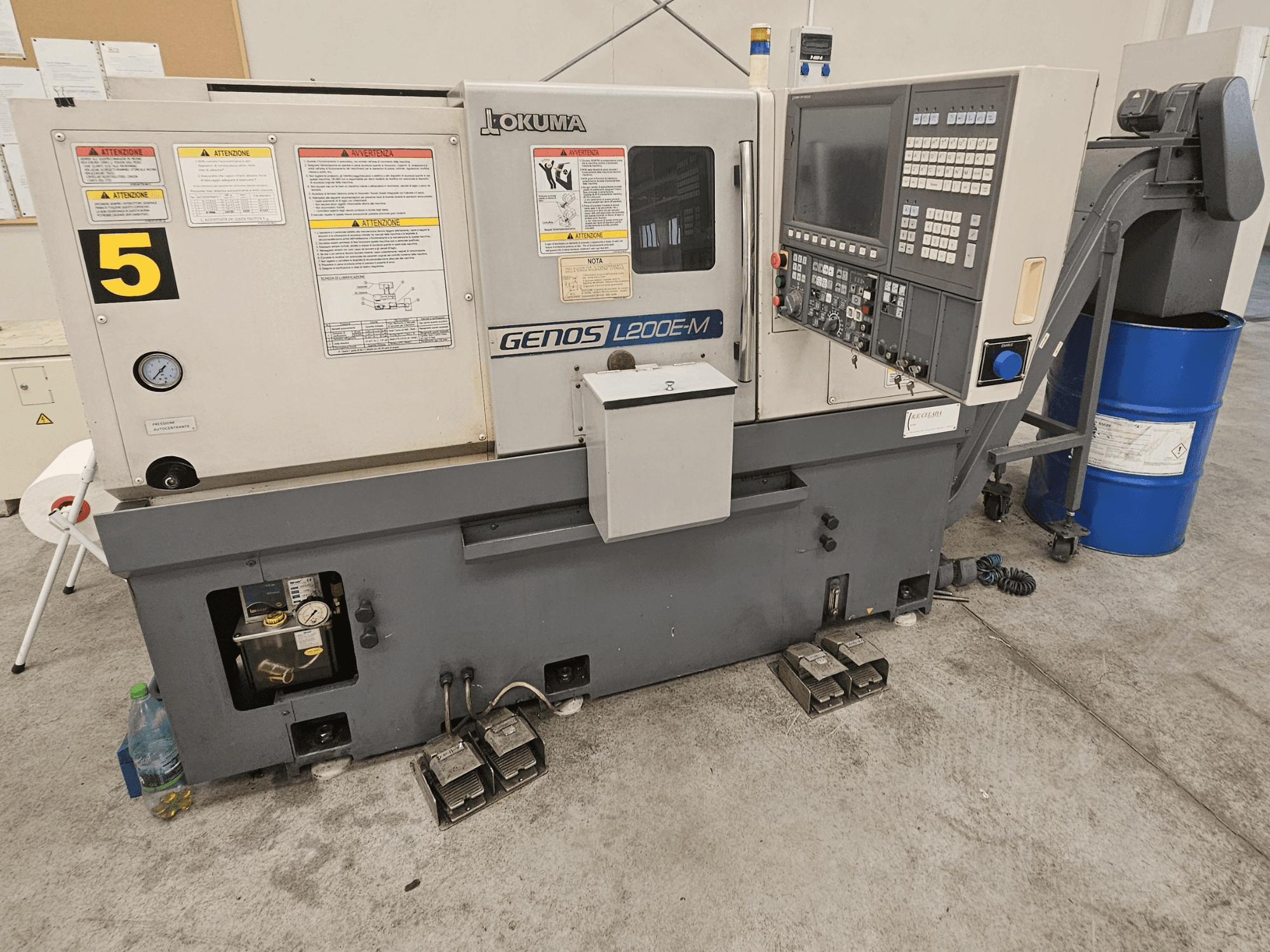 Okuma GENOS L200E-M horizontale draaimachine in vooraanzicht, met bedieningspaneel, labels en koelvloeistofvat.