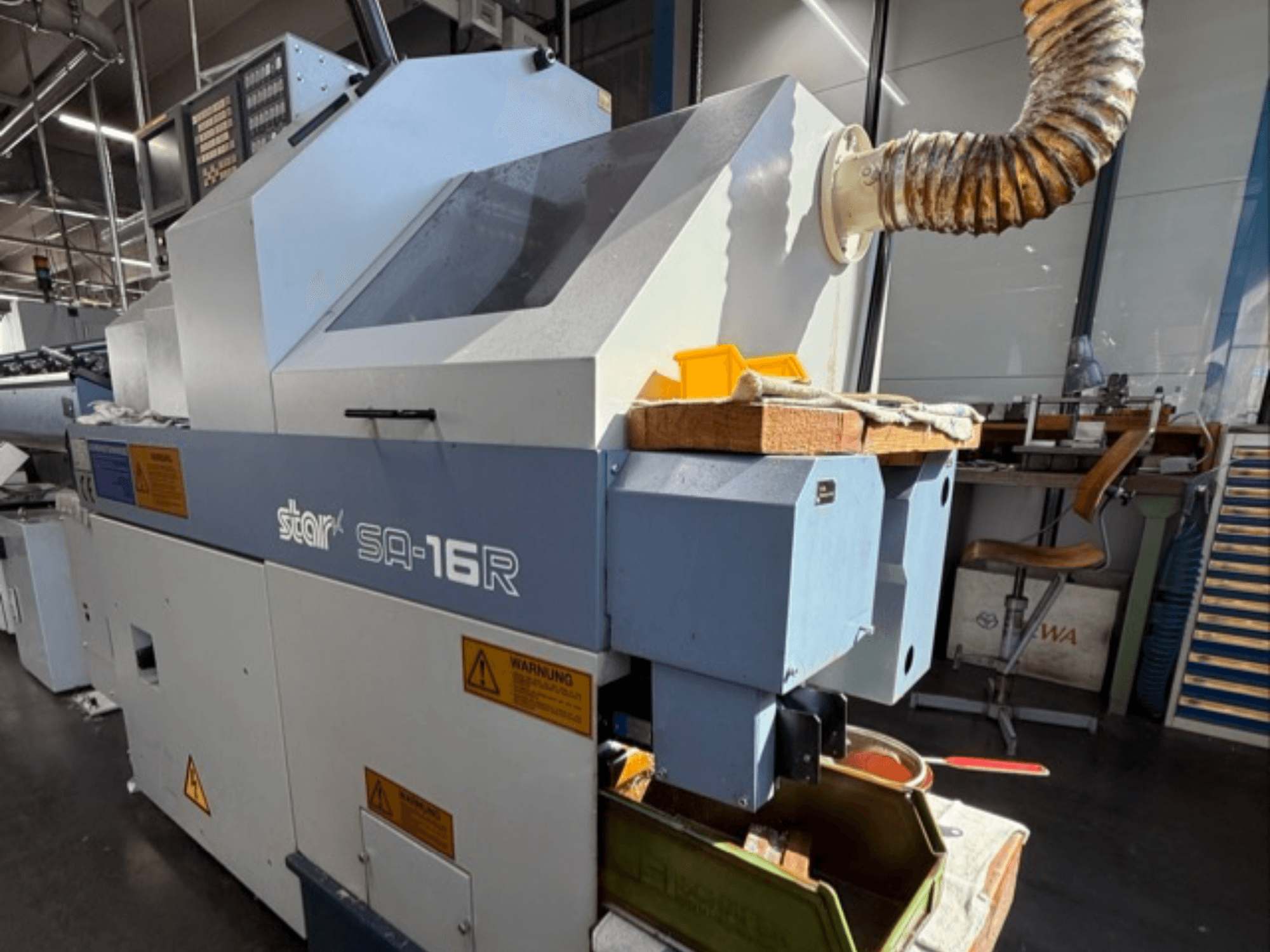Stark SA-16R machine gezien vanaf de voorkant, met een taps toelopende uitlaat en werkruimte met gele gereedschappen en waarschuwingslabels.