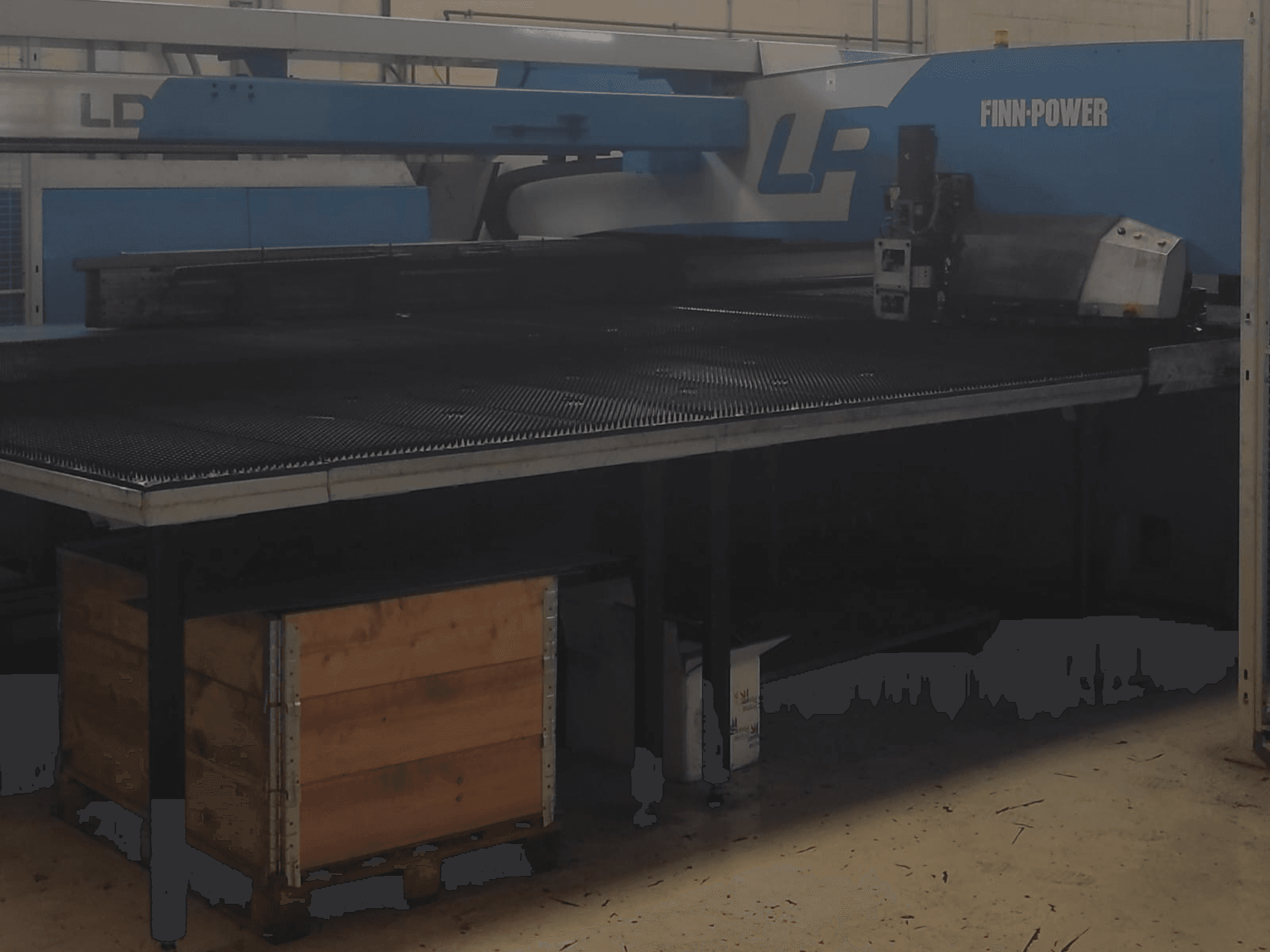 Finn-Power LP snijmachine in een fabriek, vooraanzicht met een metalen tafel met structuur en houten kist eronder.